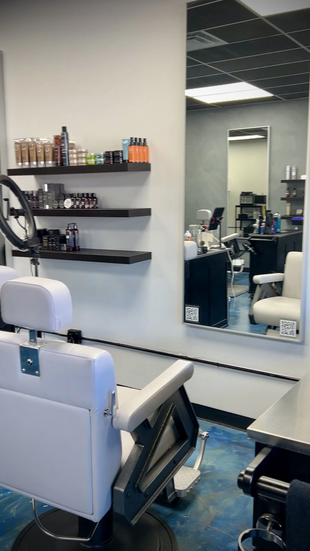 A clean and modern barber or beauty salon with a white treatment chair, a large mirror, and shelves stocked with hair or skincare products.