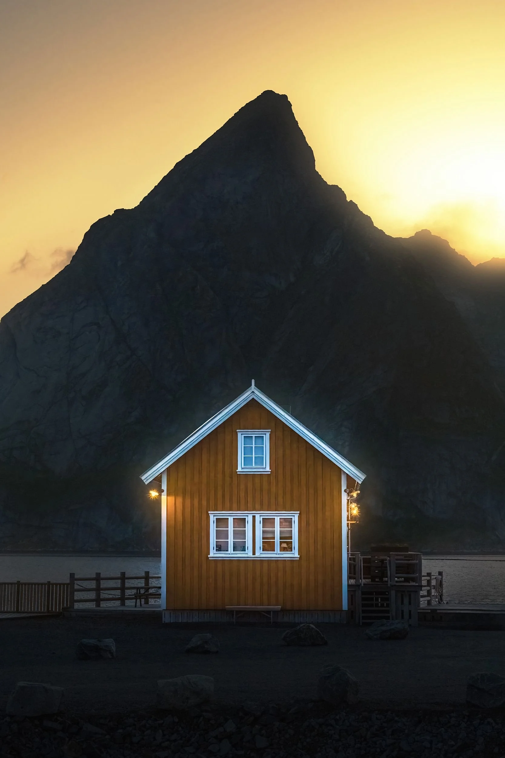 A small wooden house with white trim at sunset, with a mountain in the background.