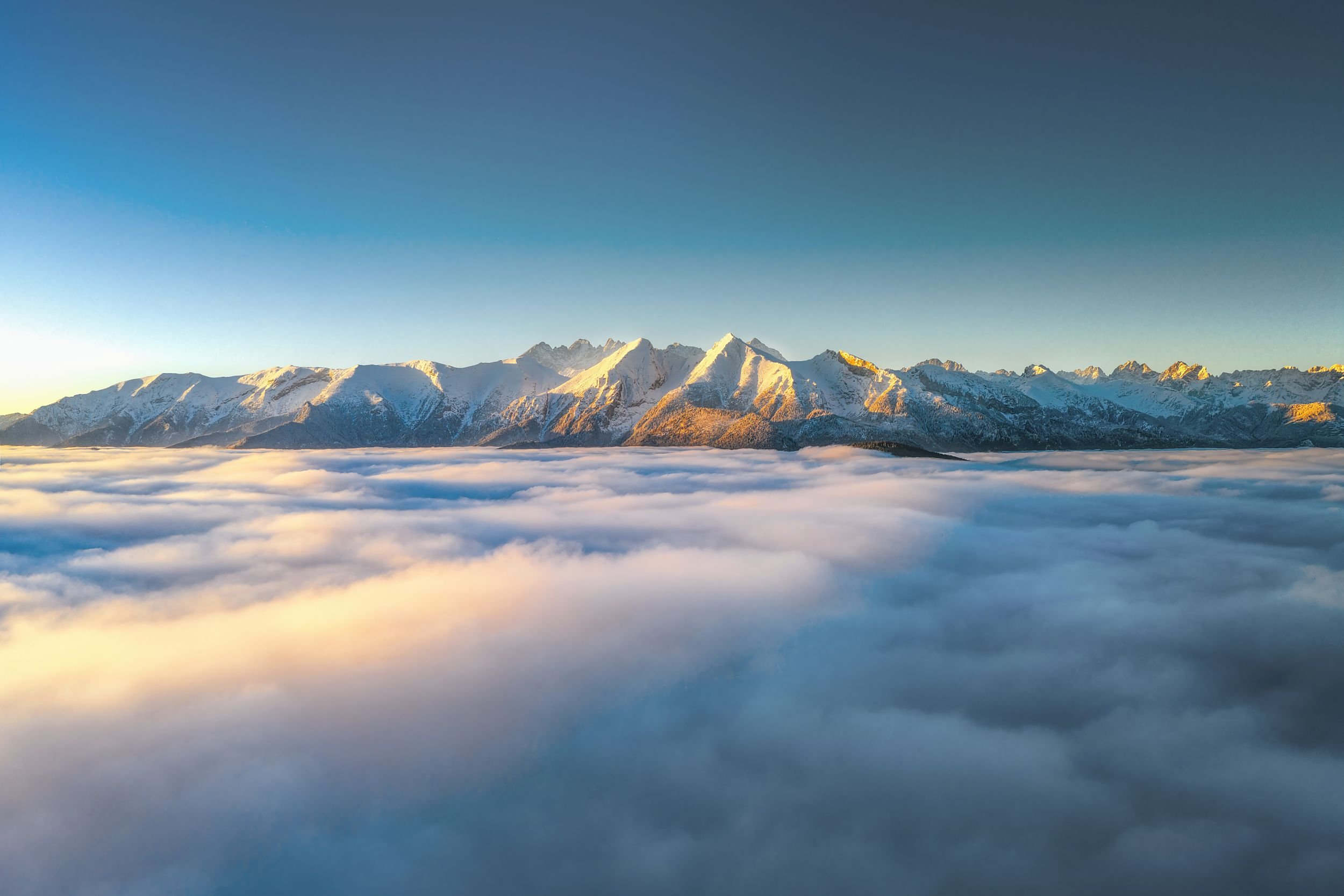 Snow-capped mountains with clouds below and a clear blue sky above in a scenic landscape.