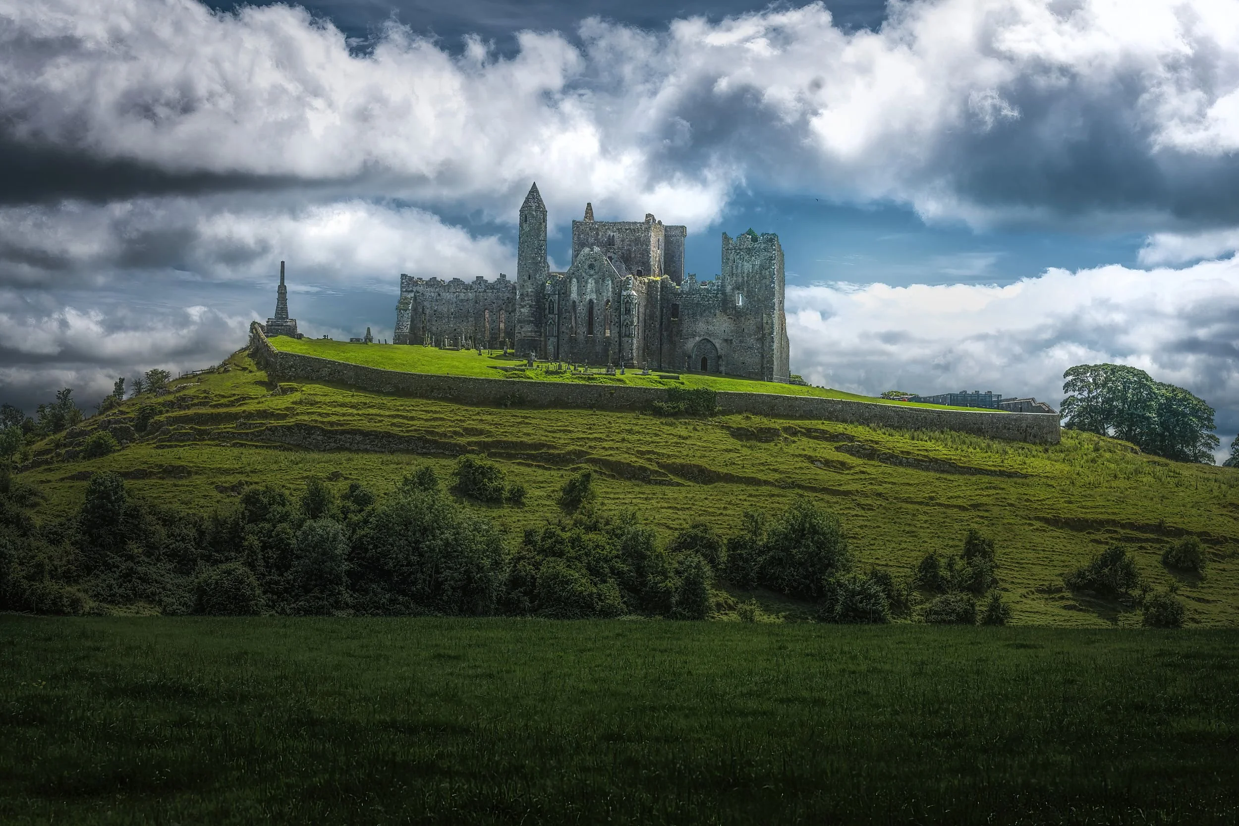 A medieval castle situated on a grassy hilltop, under a cloudy sky.
