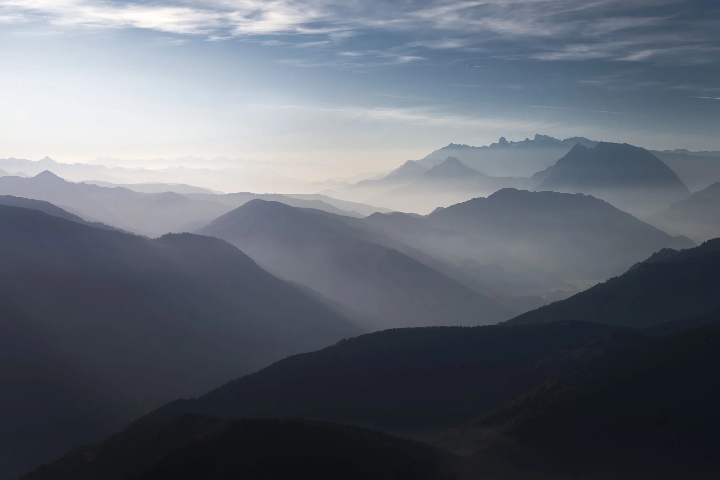 Mountain range with layered, foggy peaks under a partly cloudy sky.
