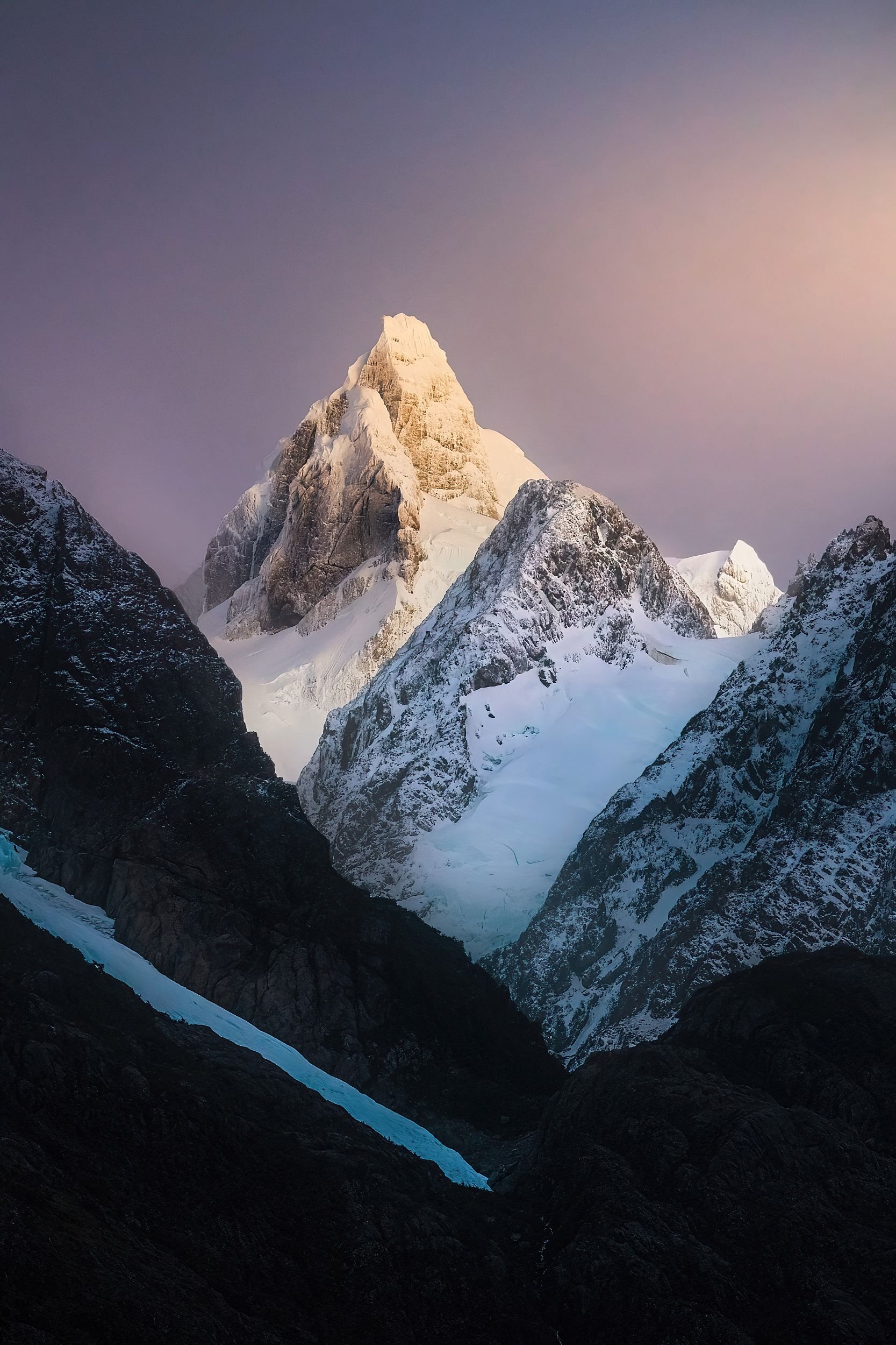 Snow-covered mountain peak at sunset or sunrise with a clear sky.