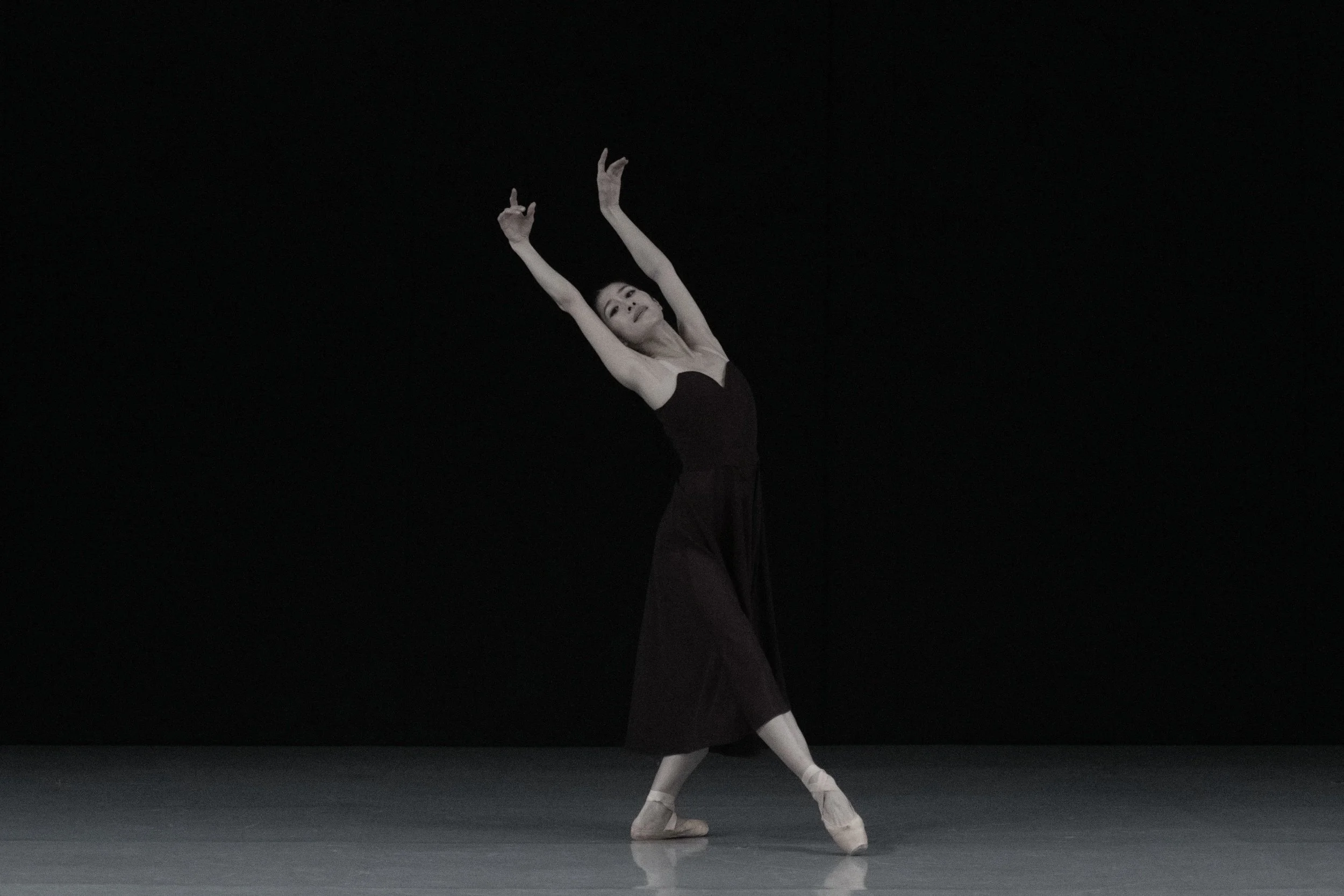 A dancer slides along the floor, hands overhead and a mysterious expression crosses her face.
