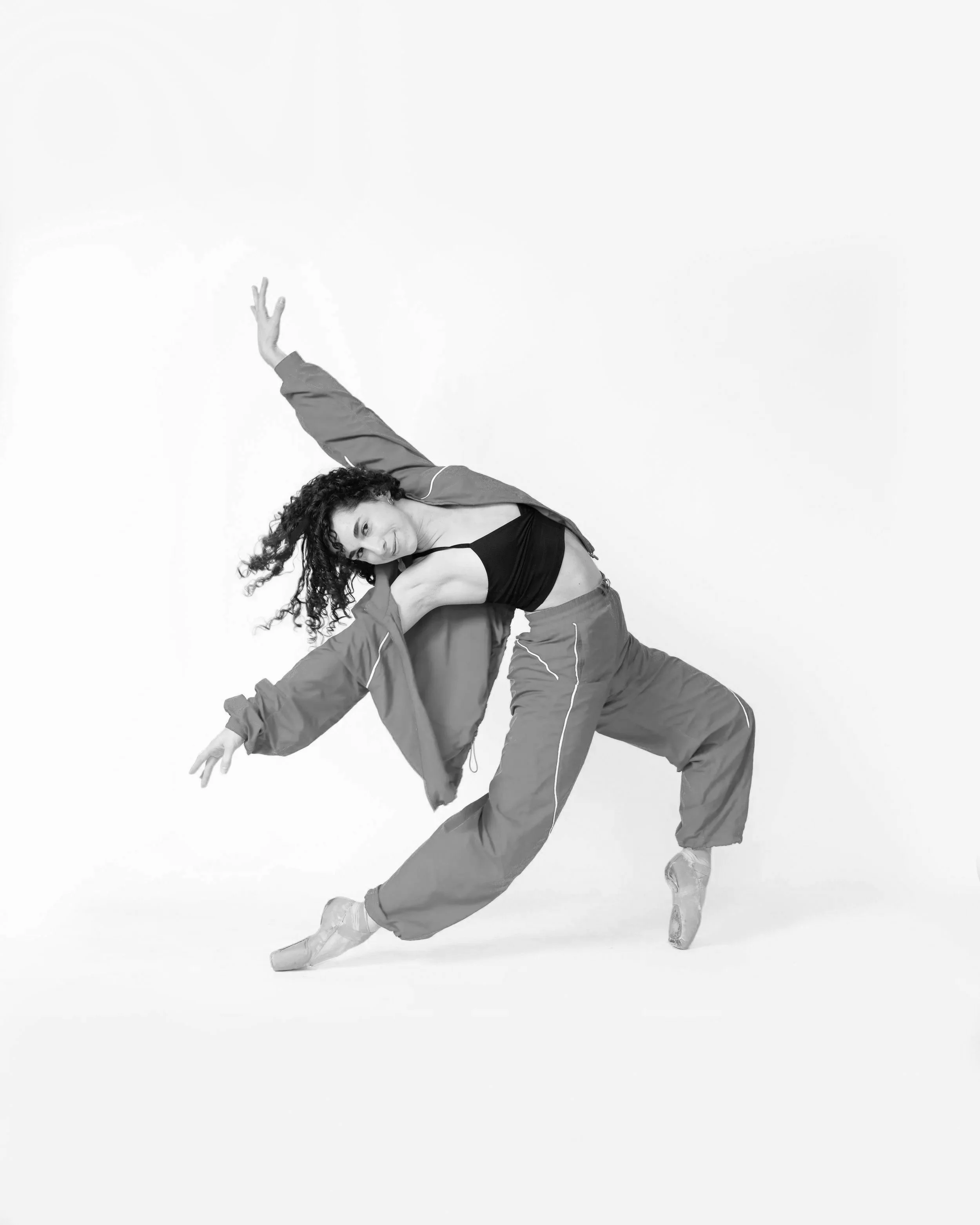 A smiling, curly haired dancer in gym clothes folds over backwards.