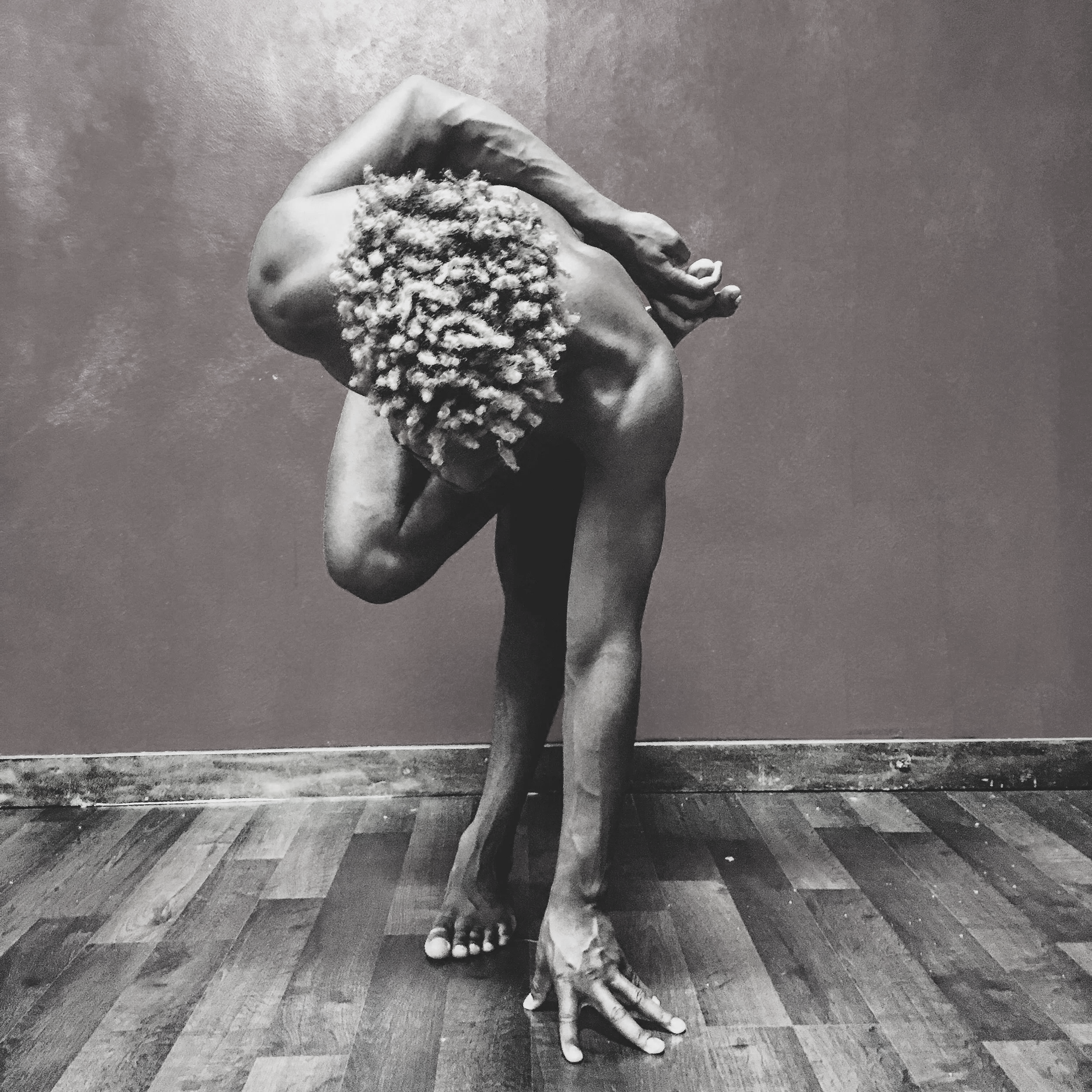 A dancer folds forward over one leg, fingertips touching the floor, neither face nor clothing visible.