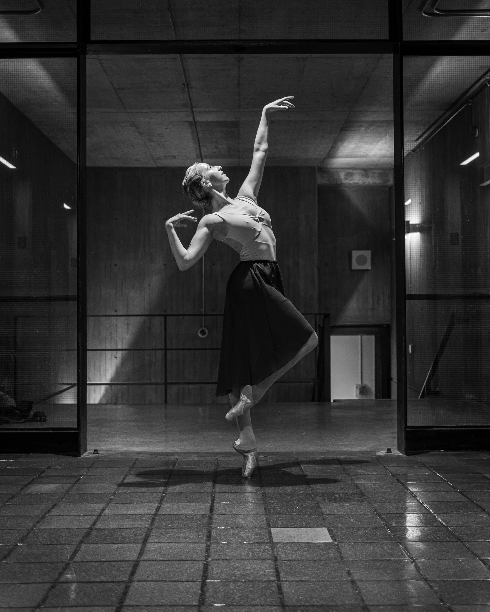 A dancer standing en pointe in cou de pie inside of Boston City Hall, soft in contrast to the extremes of the architecture.