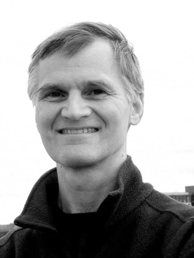 A male presenting dancer with short hair smiles at the camera.