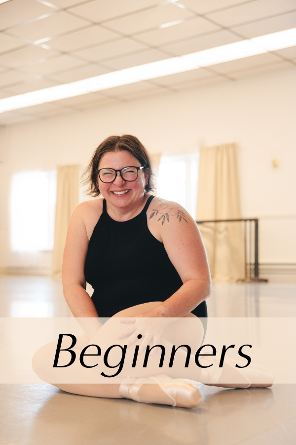 A smiling woman with glasses and a tattoo on her shoulder sits on the floor before class.