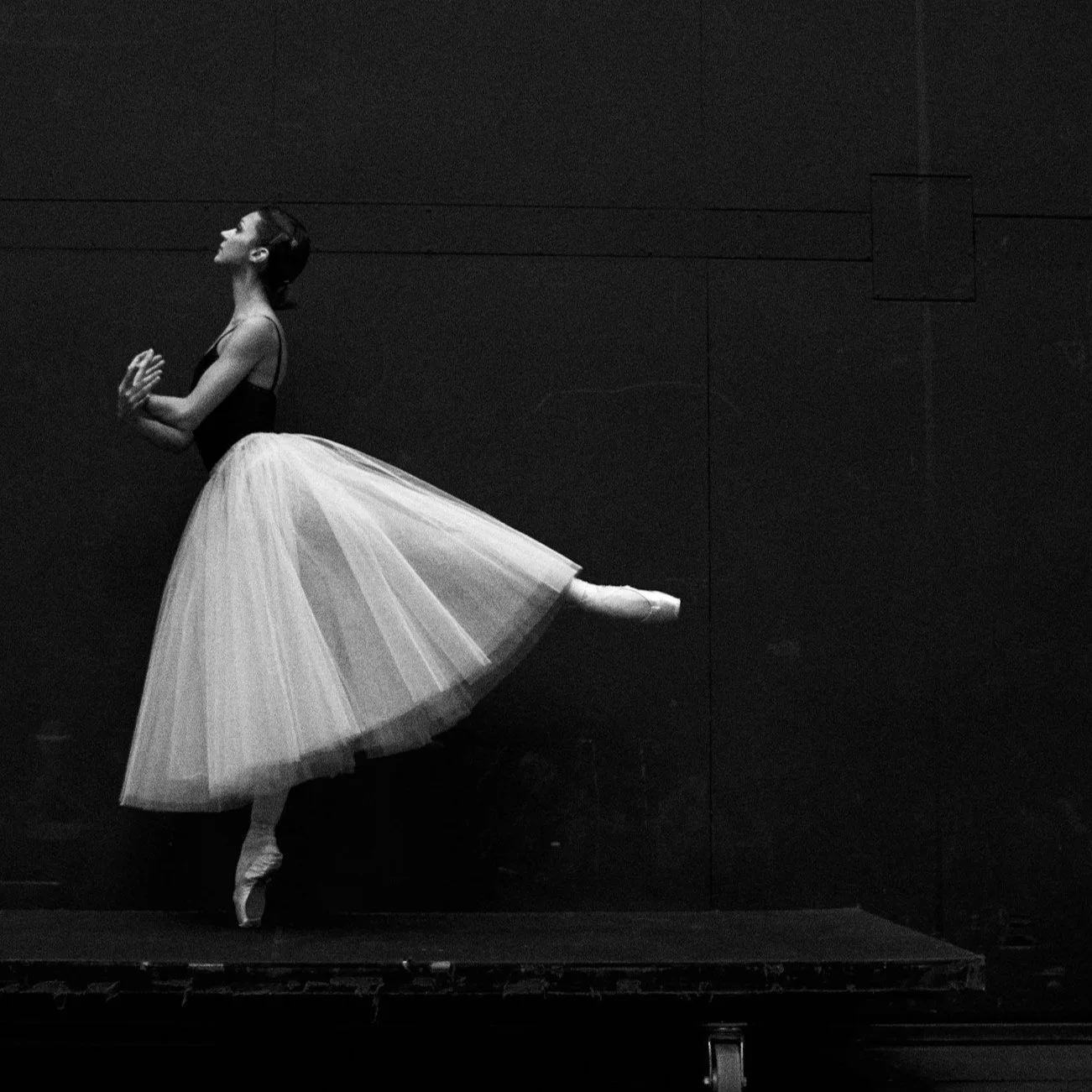 A dancer stands on pointe in arabesque, looking up wistfully.