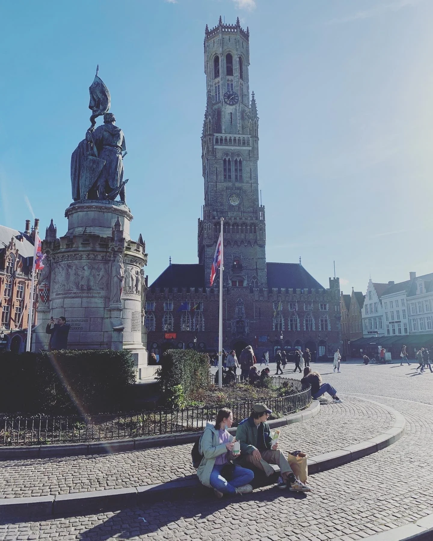 Photograph of a couple sitting in a city square with medieval architecture in the background.