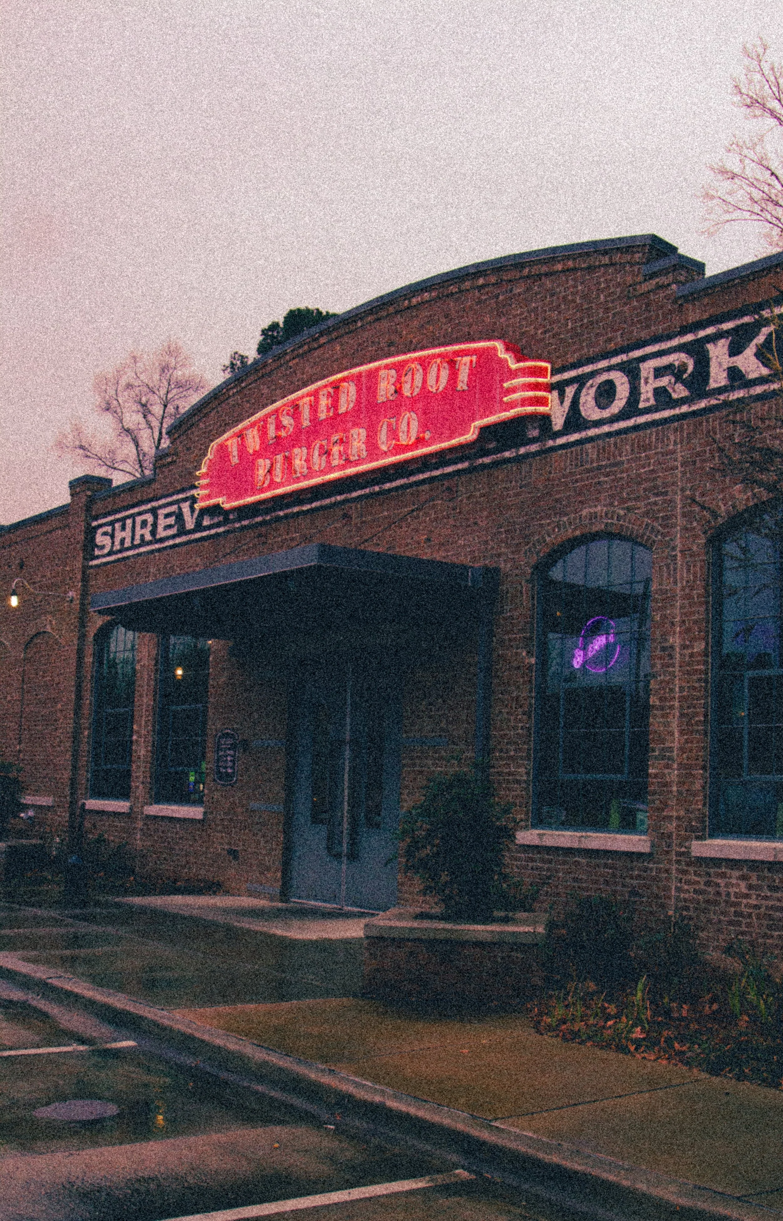 Artistic photograph of restaurant’s front entrance. Overhead neon sign displaying Twisted Root Burger Co.