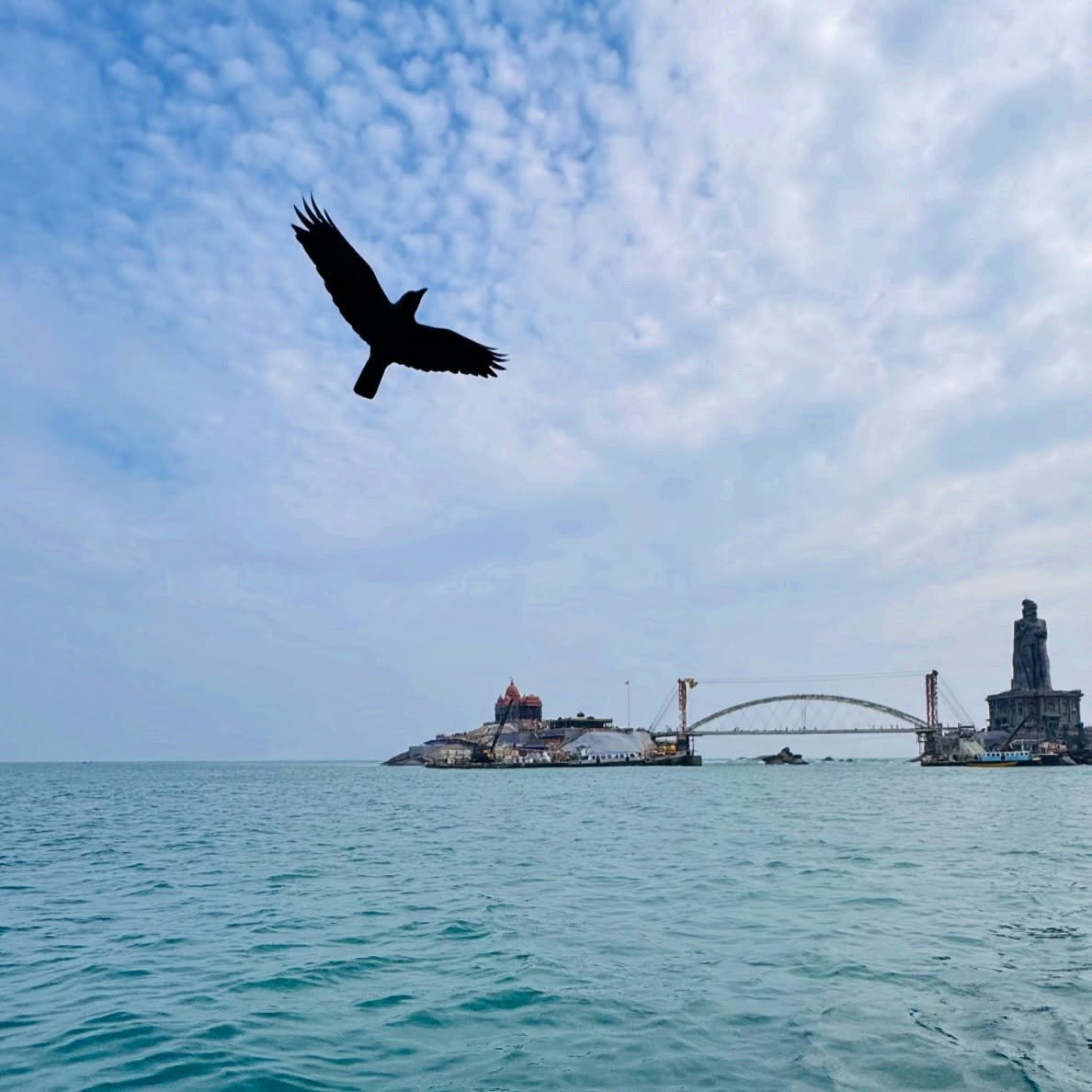 ..::F L Y::..
.
.
A lone bird soars through the endless blue,
Where the ocean gleams with a tranquil hue.
The island stands, a timeless shrine,
Amid the waves, a sacred line.

The temple&rsquo;s dome and the statue&rsquo;s gaze,
Rise steadfast throug