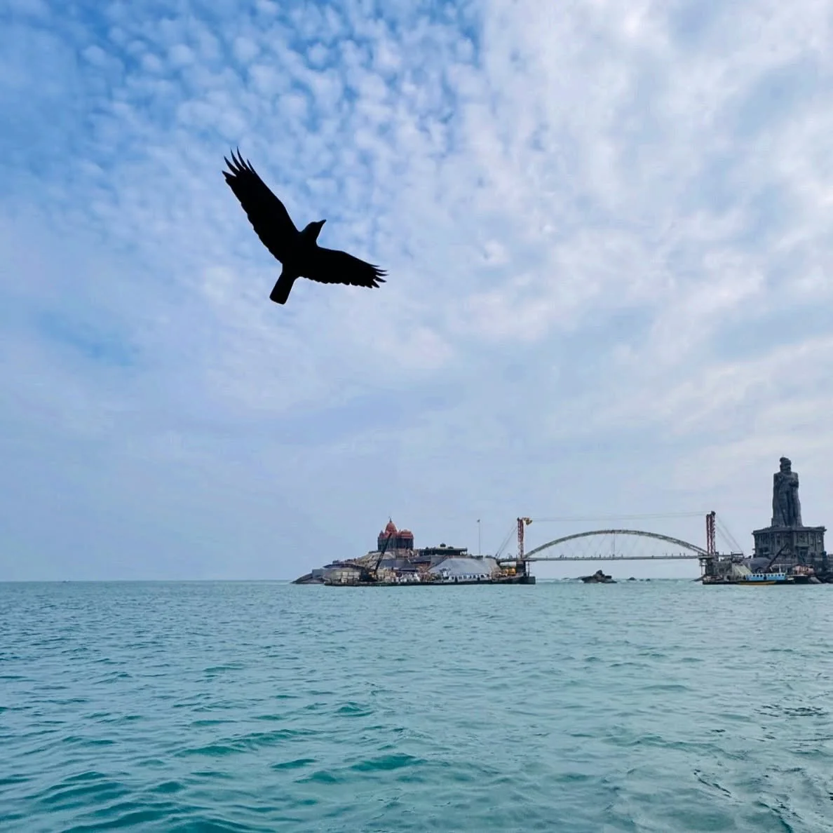 ..::F L Y::..
.
.
A lone bird soars through the endless blue,
Where the ocean gleams with a tranquil hue.
The island stands, a timeless shrine,
Amid the waves, a sacred line.

The temple&rsquo;s dome and the statue&rsquo;s gaze,
Rise steadfast throug