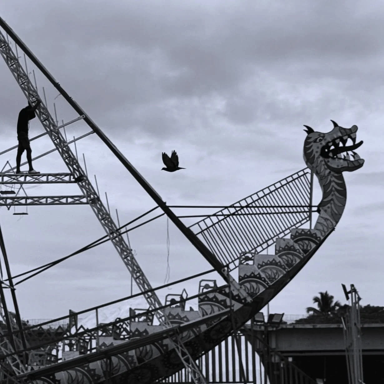 ..::C H A S E::..
.
.
A ship frozen in the sky&rsquo;s embrace,
With steel beams laced in an angular grace.
The dragon roars, though silent and still,
A ghostly sentinel over the carnival&rsquo;s will.

A lone figure climbs, suspended in thought,
His