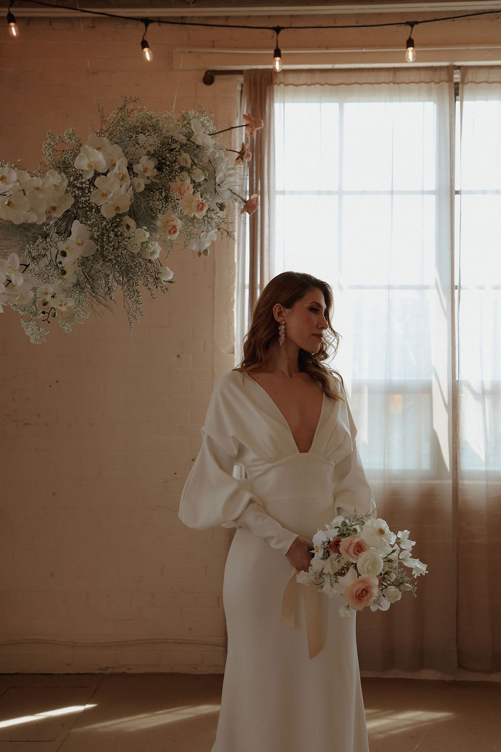 bride standing next to flower arch while holding neutral flowers for her bridal portraits