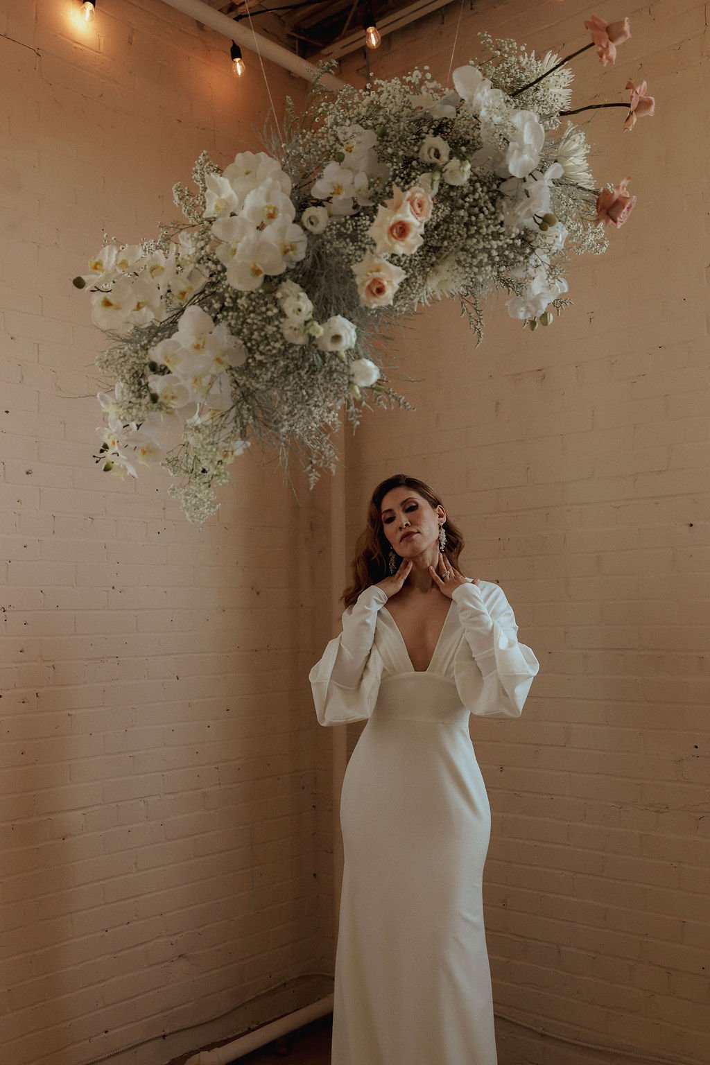bride touching neck while standing under a flower arch at a studio