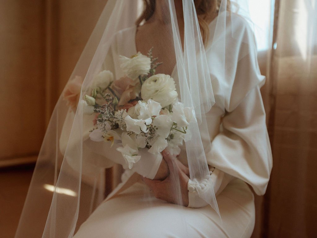 bride sitting in chair while holding flowers with viel
