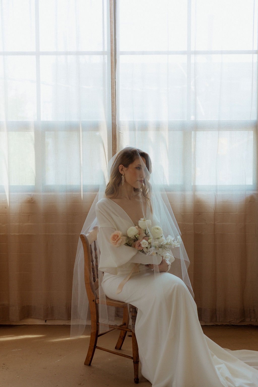 bride sitting in chair while holding flowers with viel