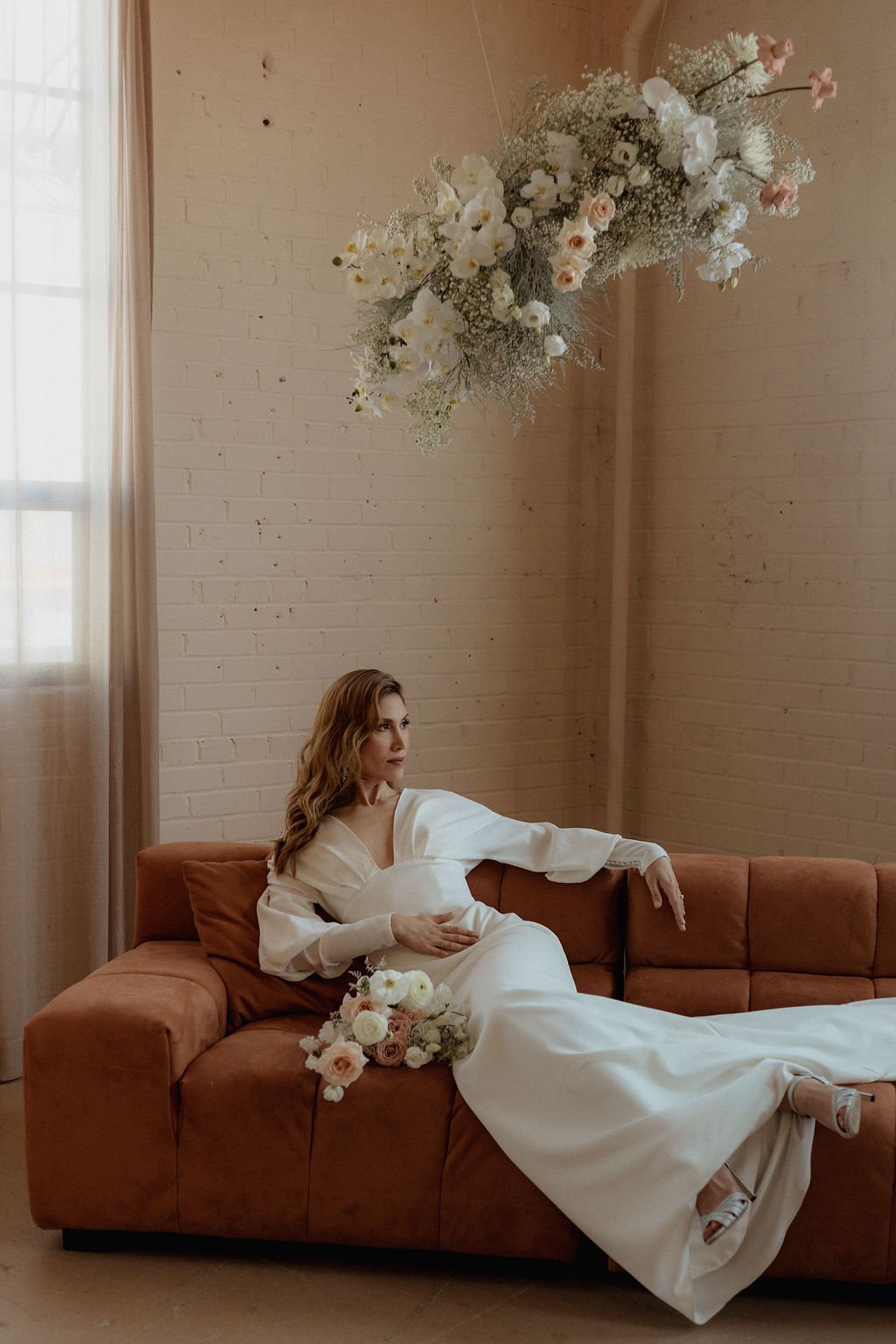 bride laying on orangey red couch while holding flowers