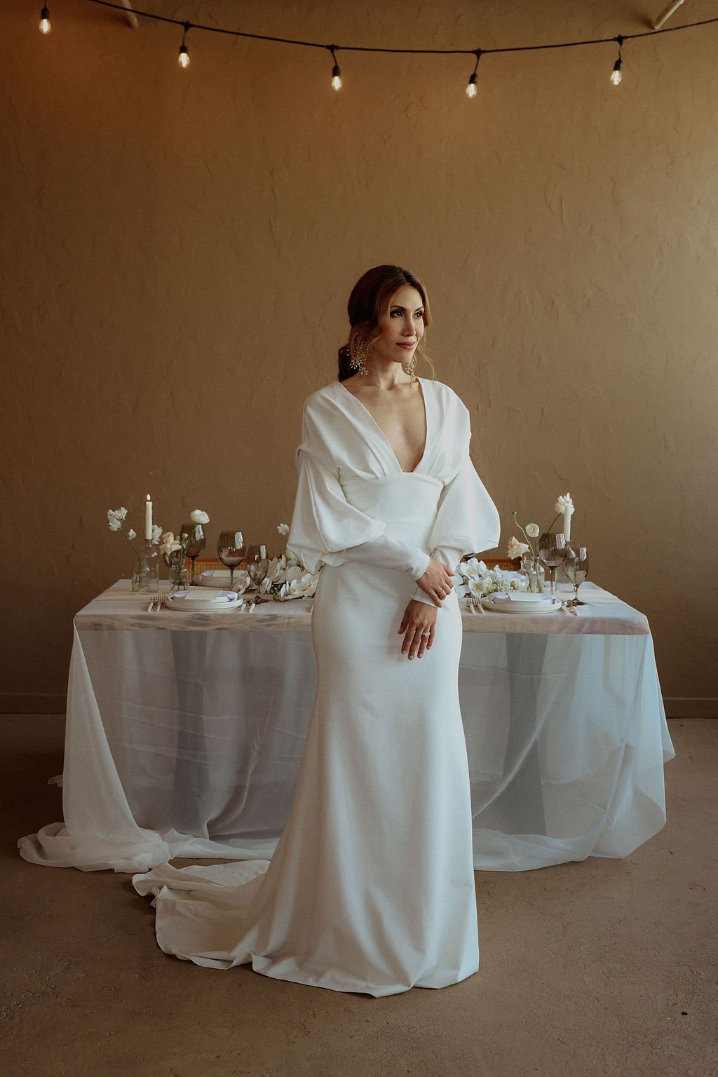 bride holding her hands in front of her while standing in front of reception table during her bridal portraits