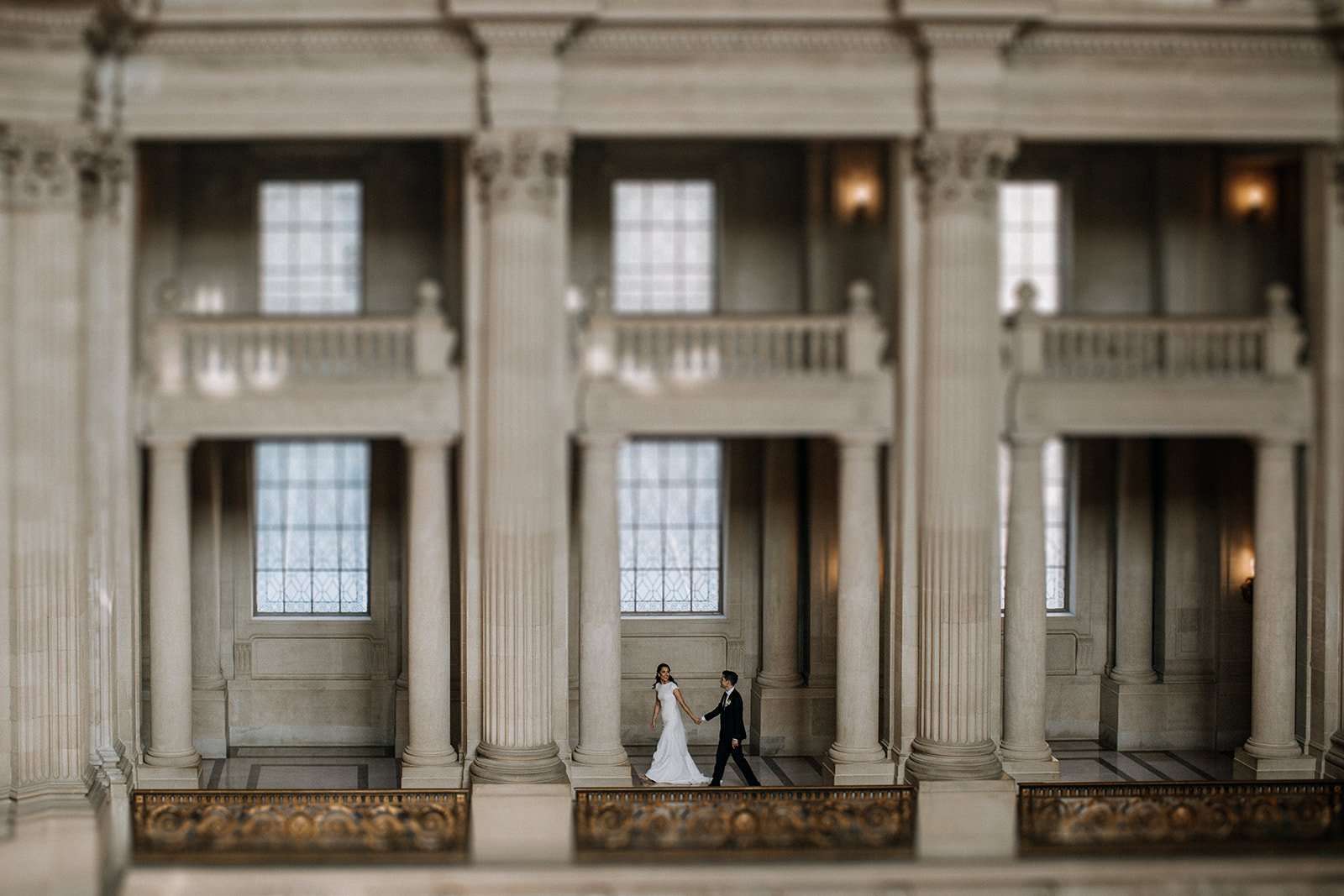  bride and groom walking holding hands in grand architecture  