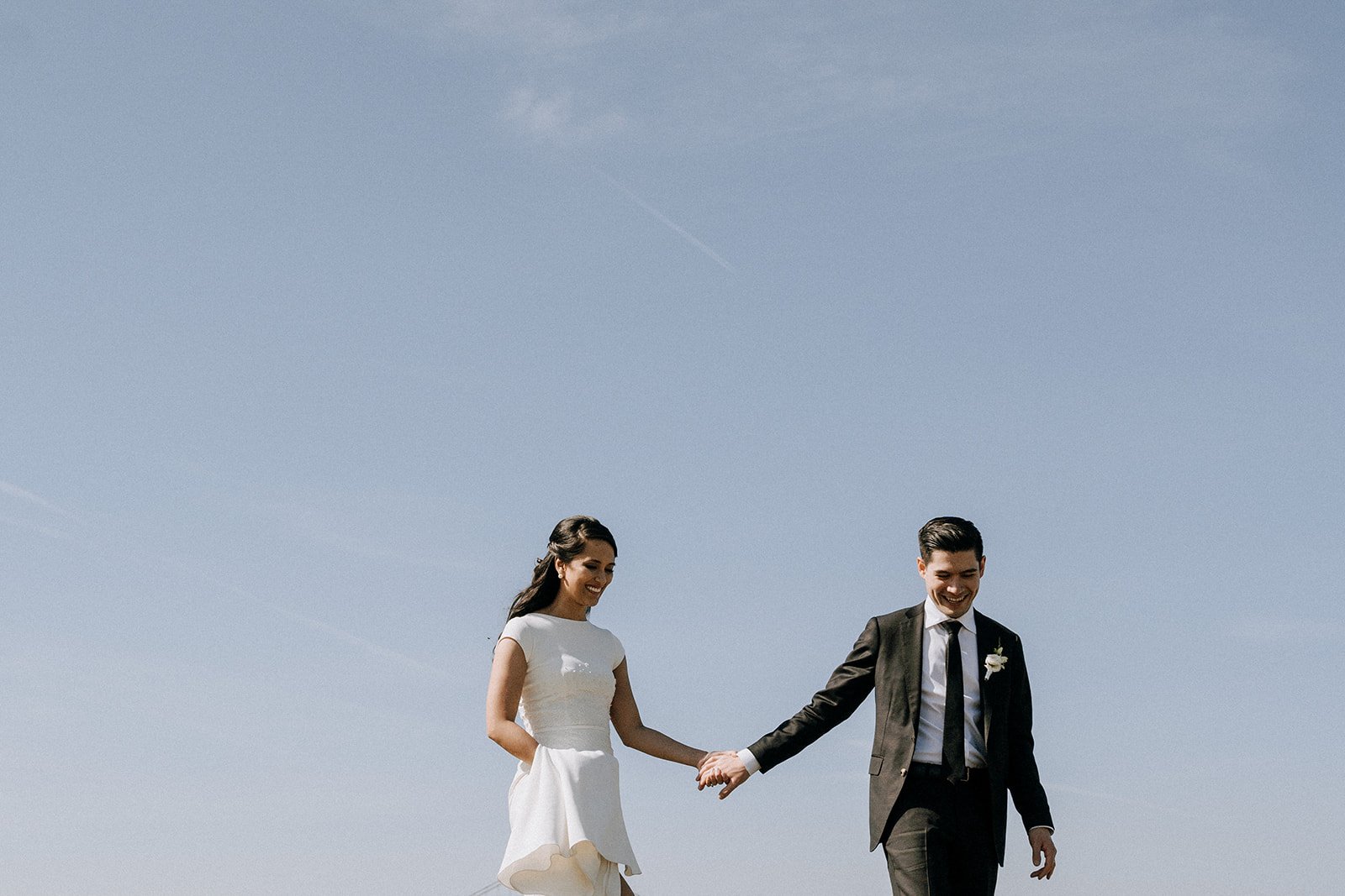  bride and groom smiling holding hands with the sky as a backdrop  