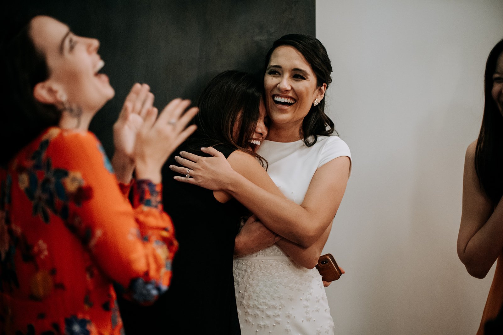  woman laughing and clapping with another woman hugging bride  