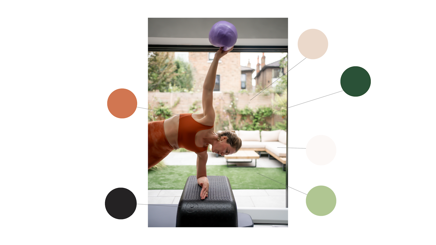 Woman performing a handstand exercise with a purple exercise ball at home gym, holding onto a black step bench, with indoor and outdoor garden views.