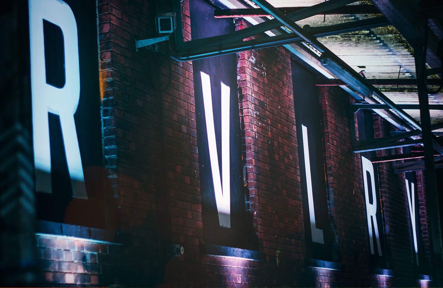 Large letters "R, V, L" on a brick wall under a metal structure.