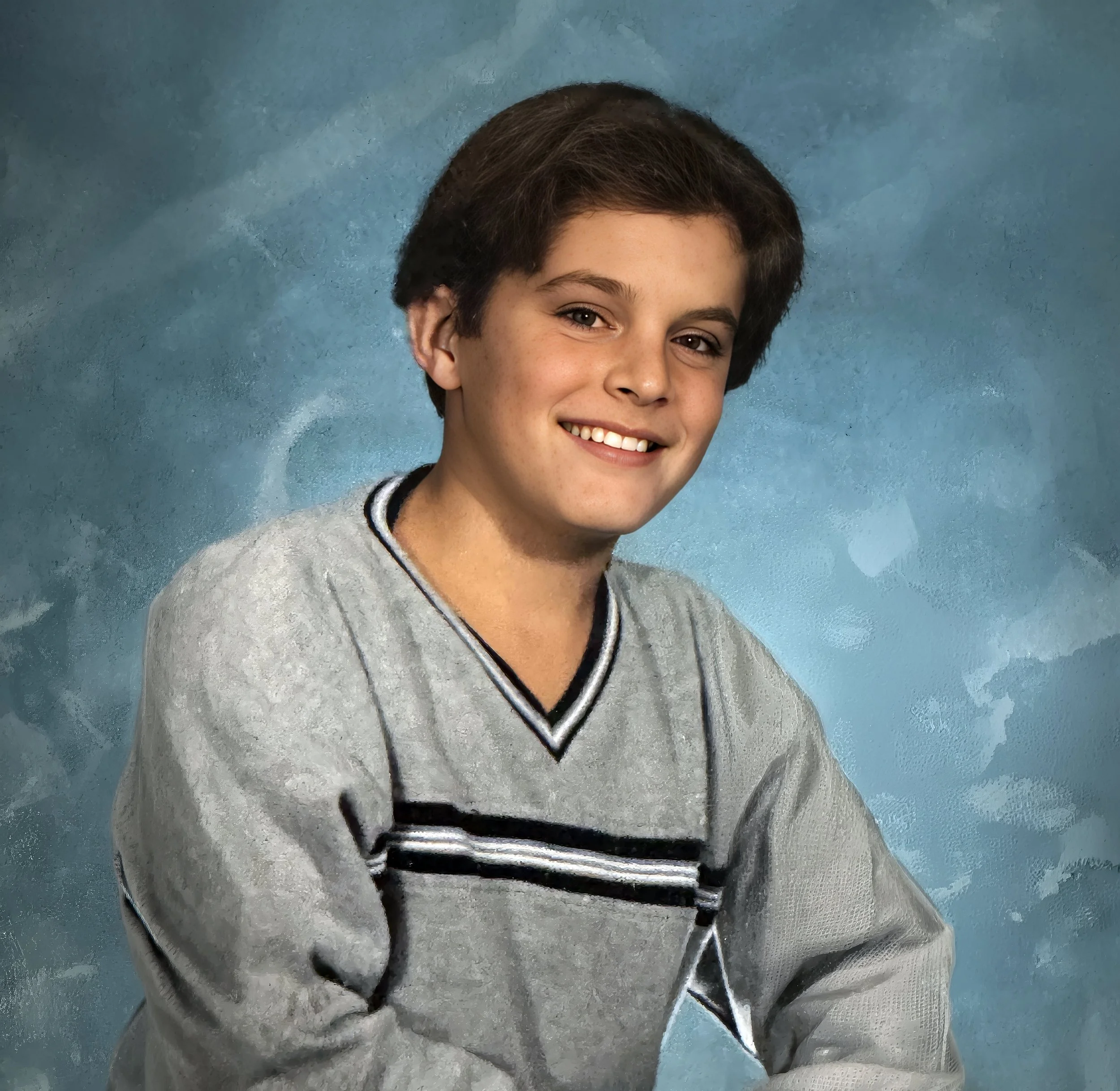 Young boy with short brown hair smiling at camera, wearing a gray sweater with black and white stripes, against a light blue textured background.