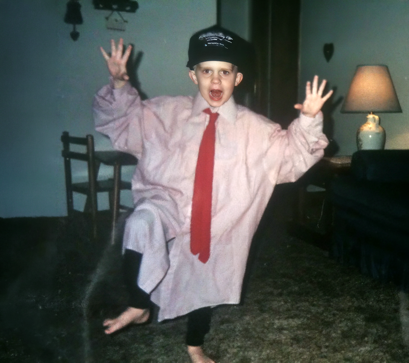 Child dressed in pajamas, tie, and hat, pretending to be a policeman, standing on one leg with arms raised in a pose of surprise or excitement in a living room.