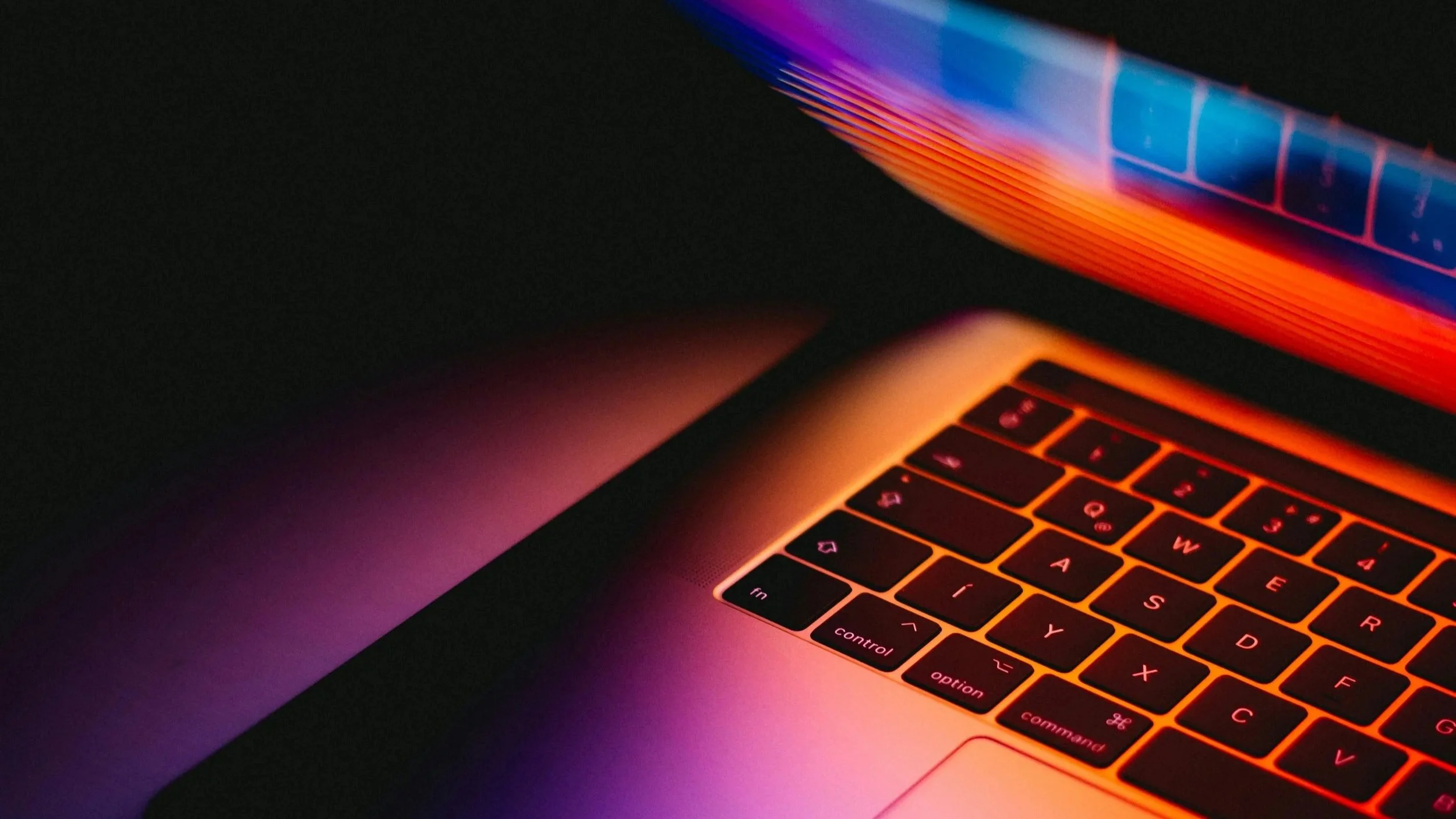 Close-up of a laptop keyboard with backlit keys glowing orange and a display showing colorful abstract lines in orange, purple, and blue.