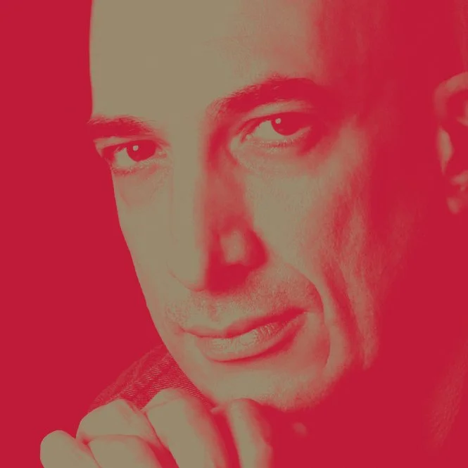 A close-up portrait of a man with piercing eyes, with a reddish filter overlay.