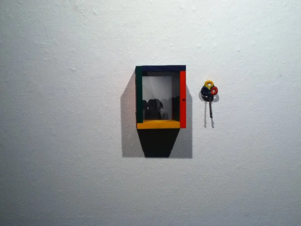 Small colorful cabinet mounted on a white wall with a dog silhouette inside and a set of keys hanging outside.