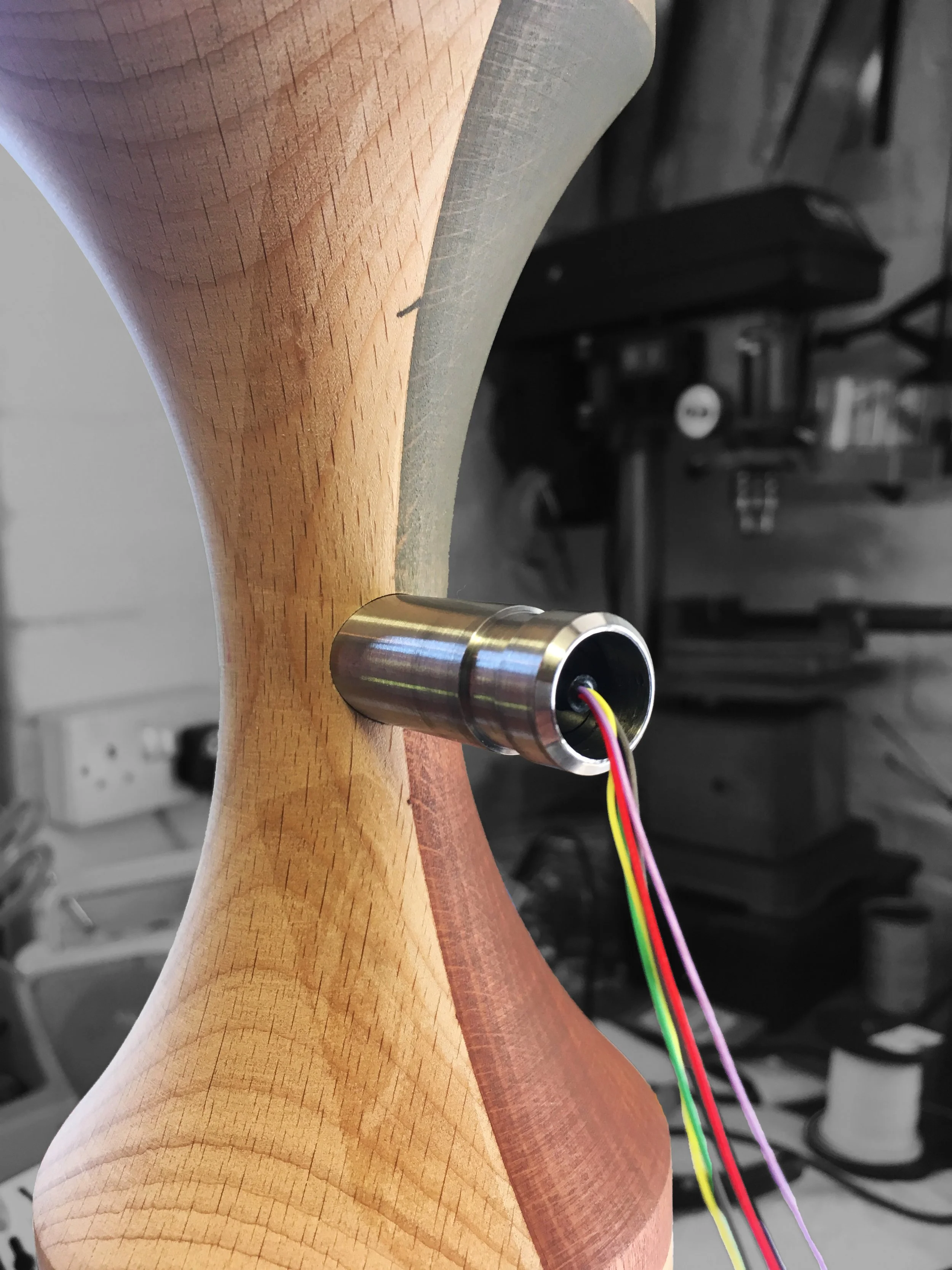 A wooden propeller with a metal hub and colorful electrical wires attached, set in a workshop environment.