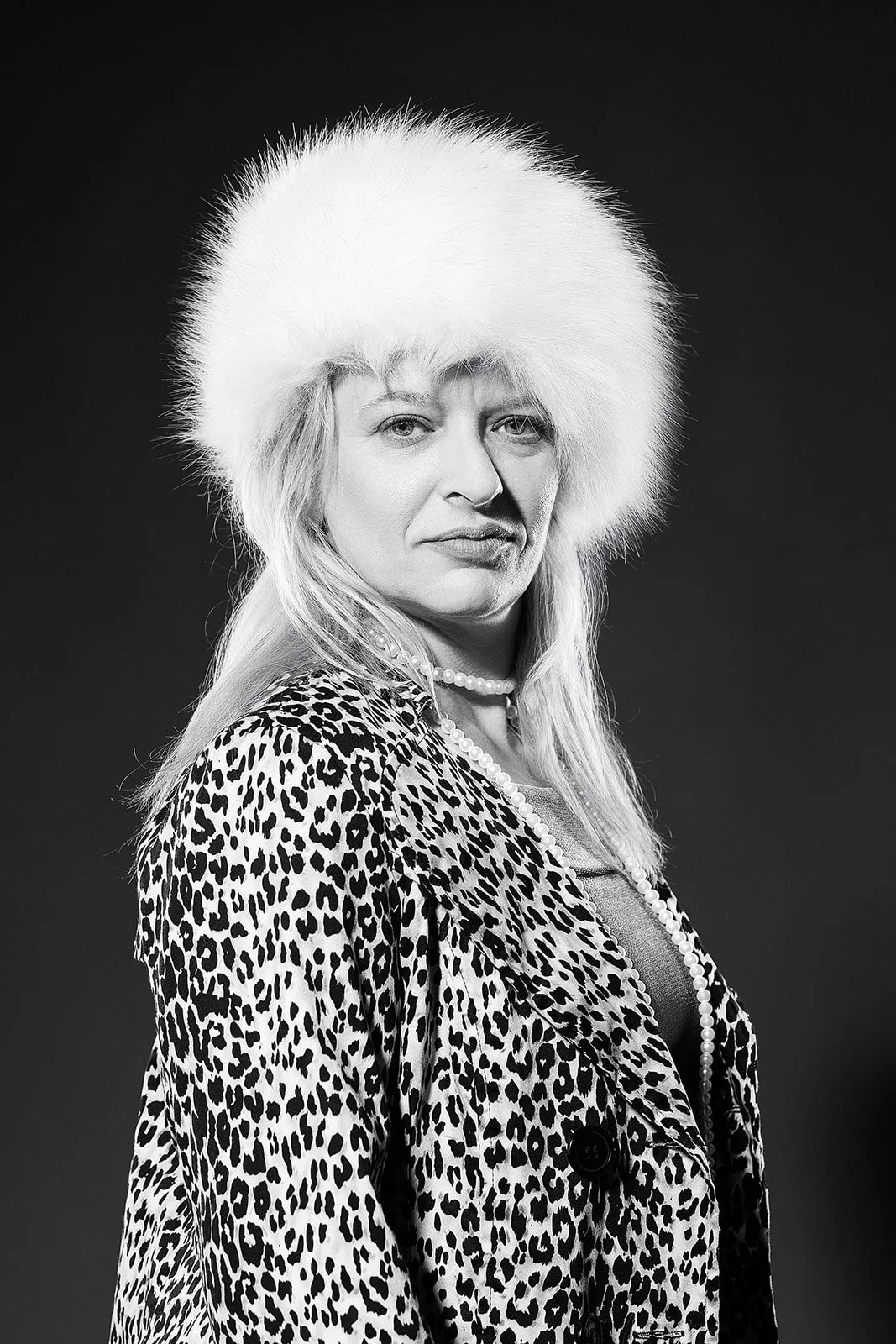 A captivating black and white Old Hollywood portrait featuring a model with a cheetah print jacket and a stylish, poofy white fur hat. The model looks into the camera with a timeless elegance, evoking the glamour of the classic Hollywood era.