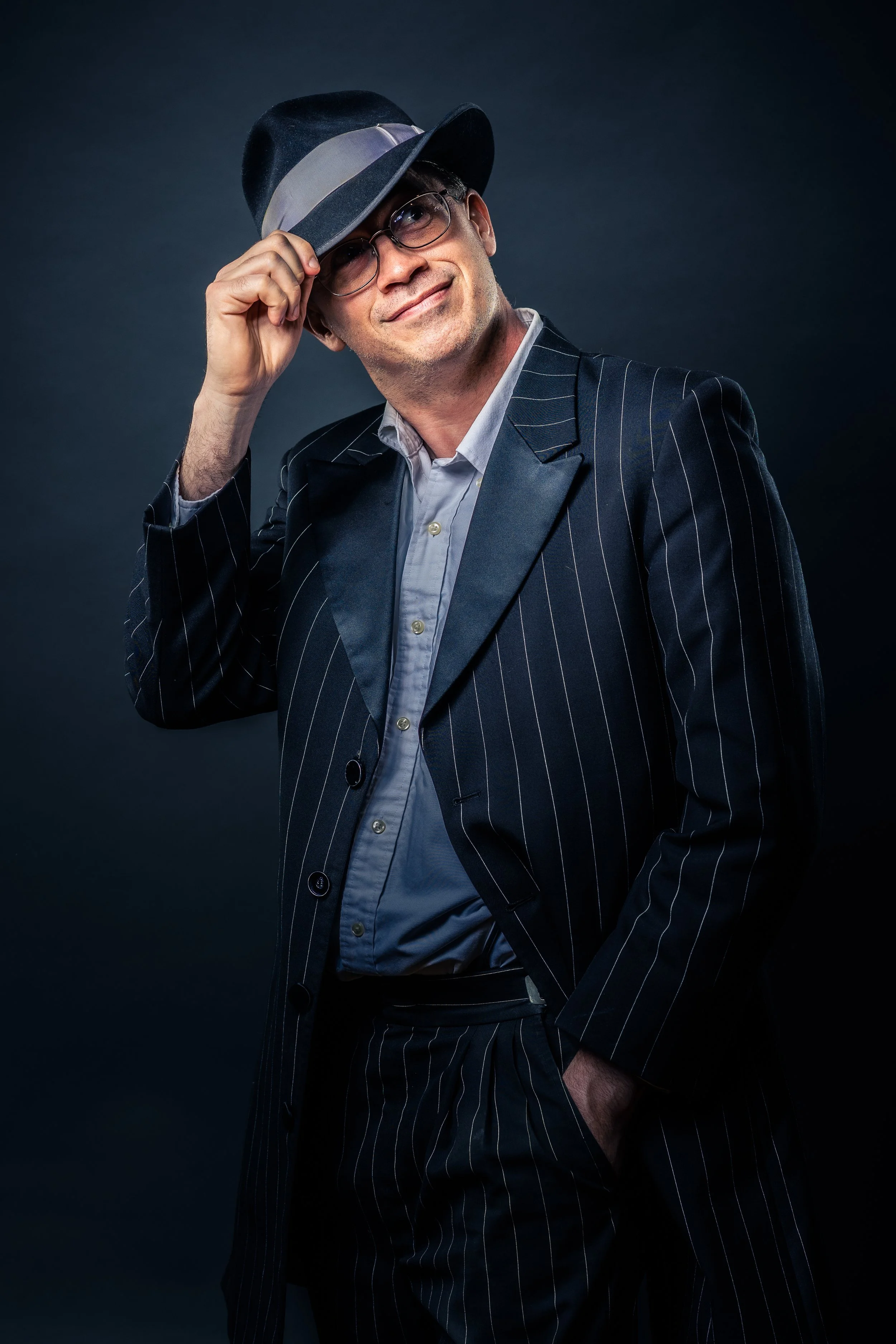 A studio portrait of a stylish man wearing a 1920's coat and fedora, exuding a classic and cheery vibe.