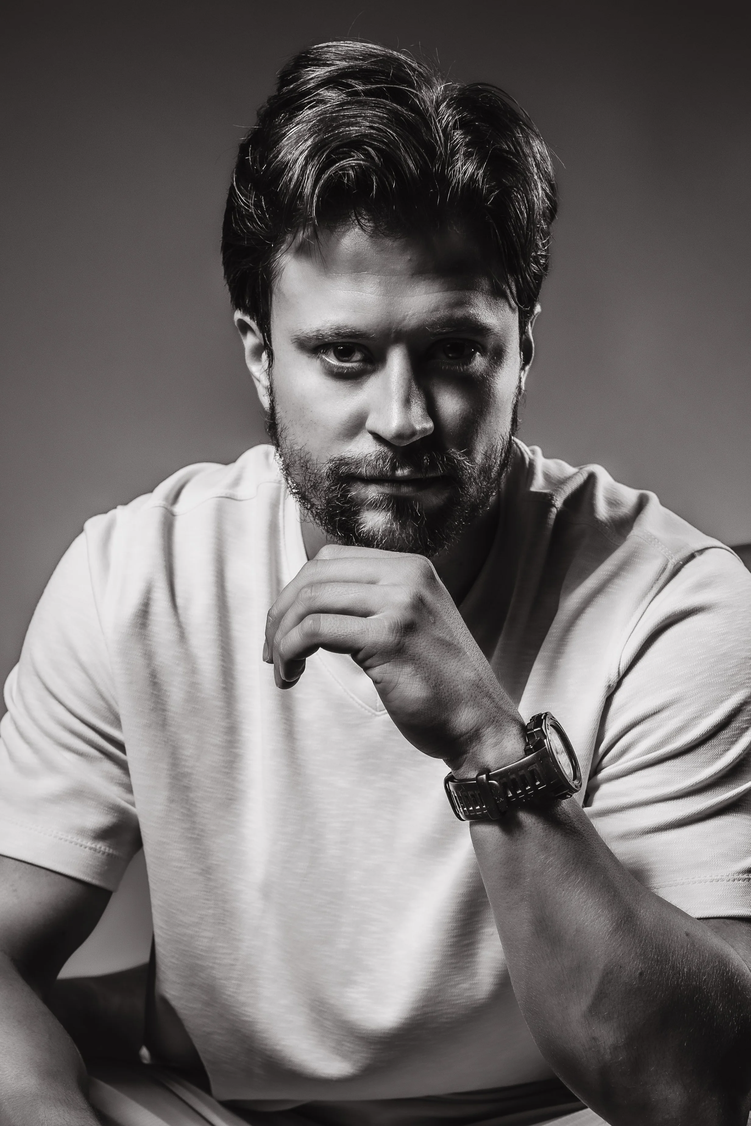 A captivating black and white portrait of a white man sitting down, showcasing his stylish watch. He maintains direct eye contact with the camera, exuding confidence and a sense of style. The photo has a commercial aesthetic, evoking a sense of sophi