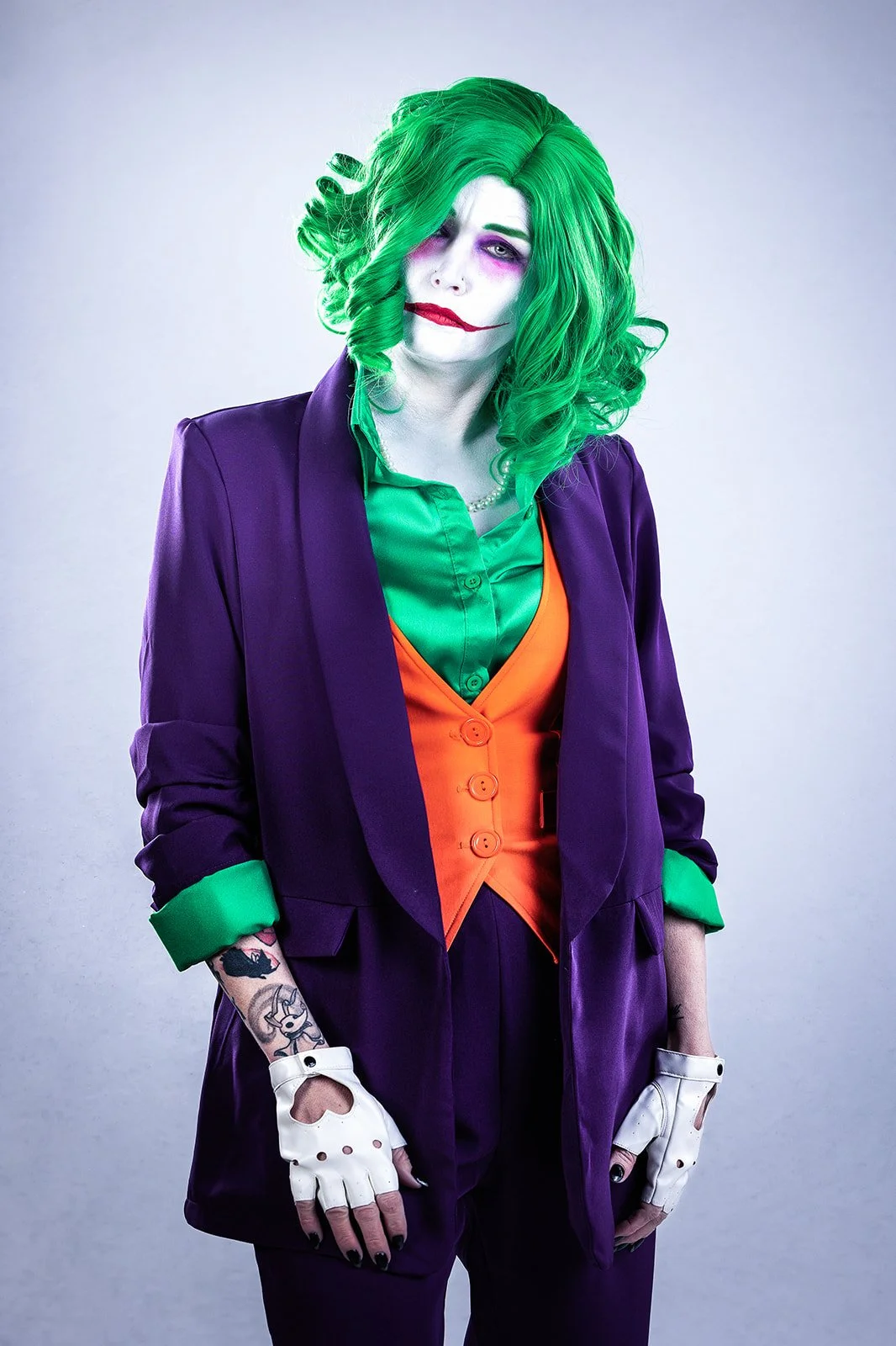 A captivating studio portrait of a woman cosplaying as the Joker from Flashpoint. She stands confidently with a somber expression on her face, embodying the complex and unpredictable nature of the character. The bright white background creates a star