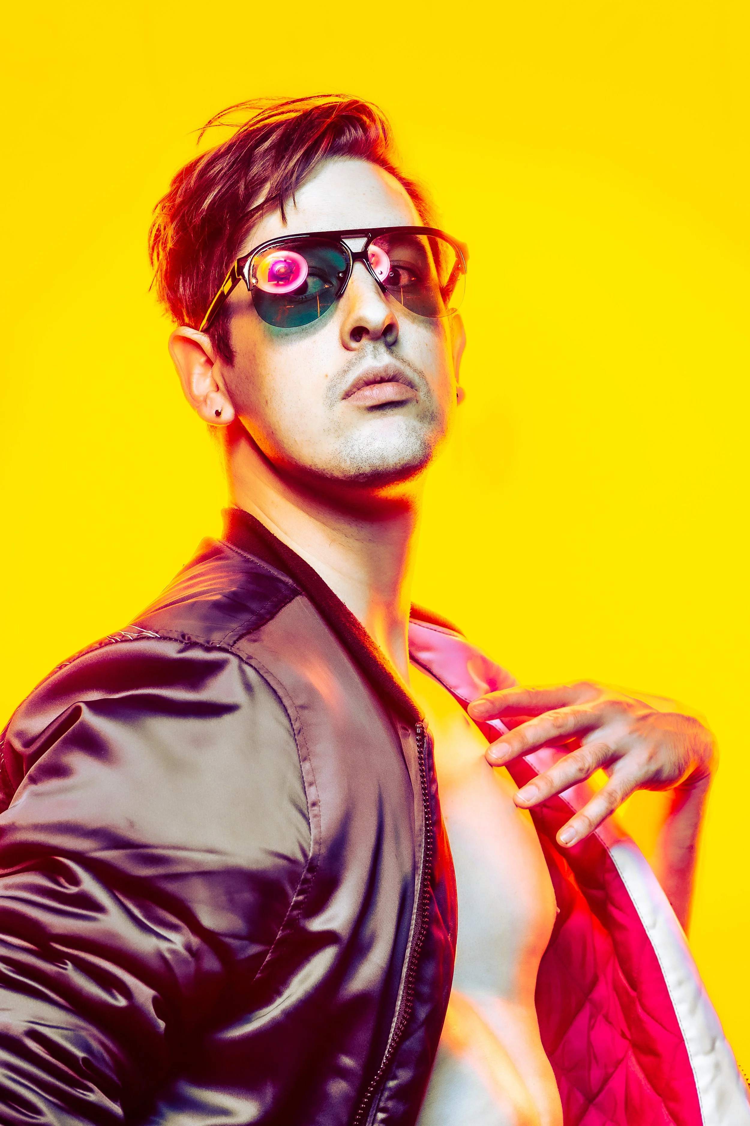 A high-key studio portrait of a white man dressed as a 1980's bad boy. The vibrant orange and yellow colors create a bold and energetic atmosphere, adding to the fashionable appeal of the image.
