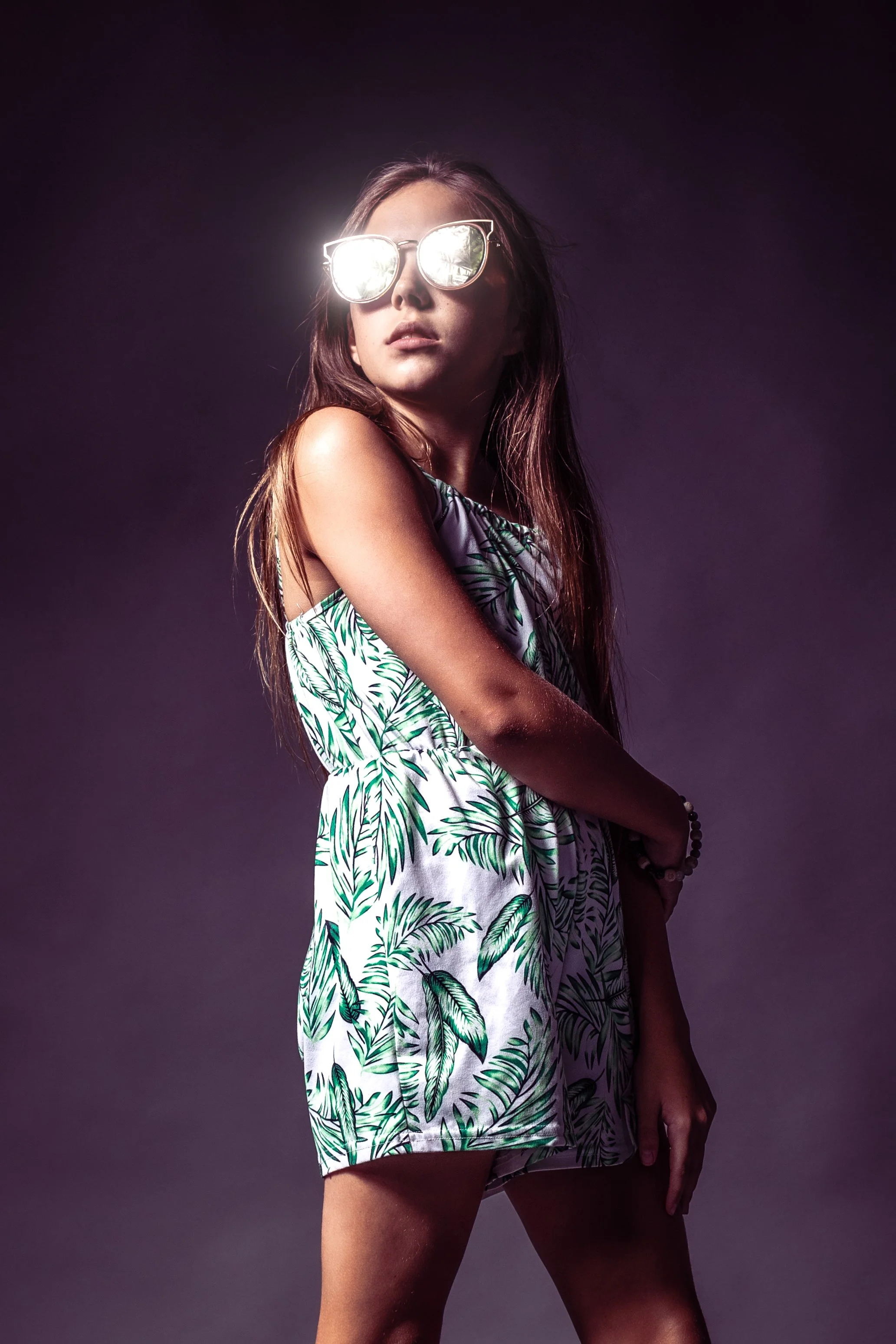 A commercial-style studio portrait of a 12-year-old white girl wearing a fashionable green and white dress. She accessorizes with sunglasses, exuding a trendy and confident vibe.