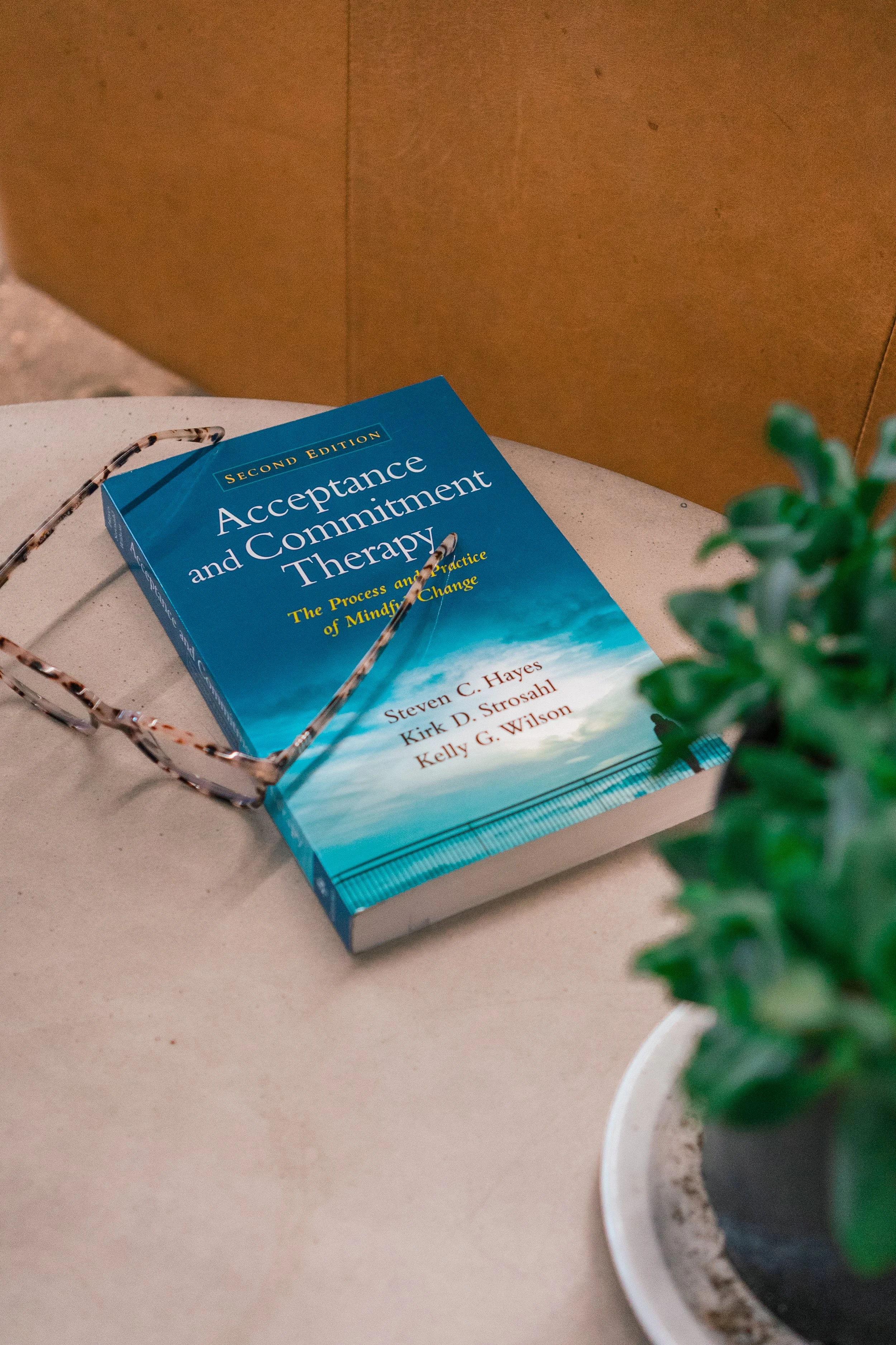 A blue book titled 'Acceptance and Commitment Therapy' resting on a side table which implies types of evidence based therapy practices.
