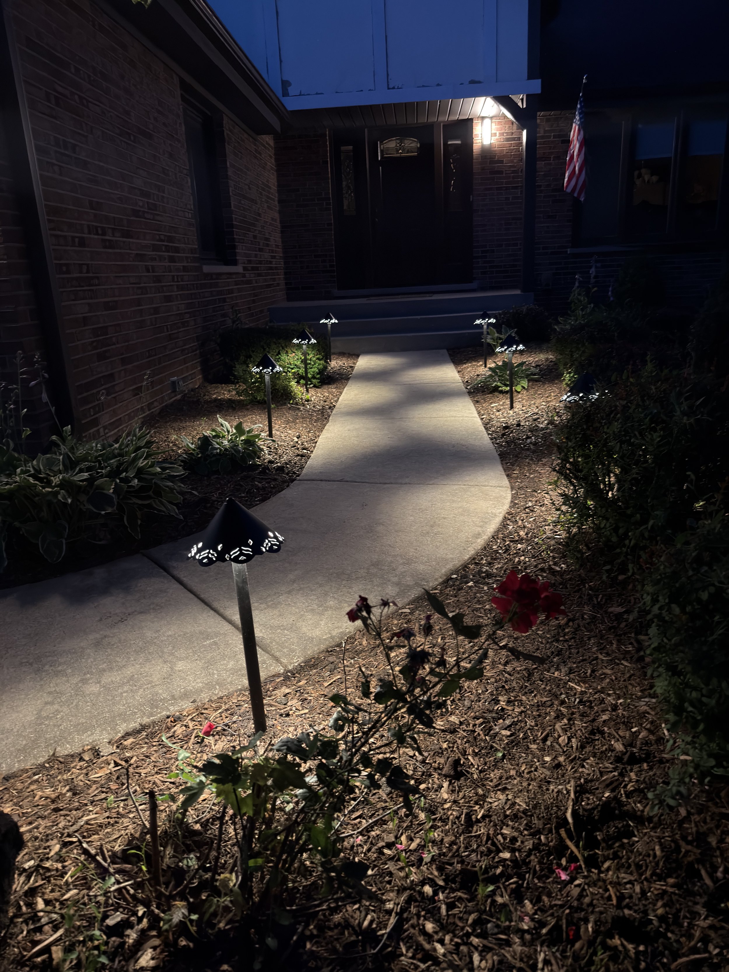 Vertical night view of a curved front walkway with a path light in the foreground and a brick entrance beyond.