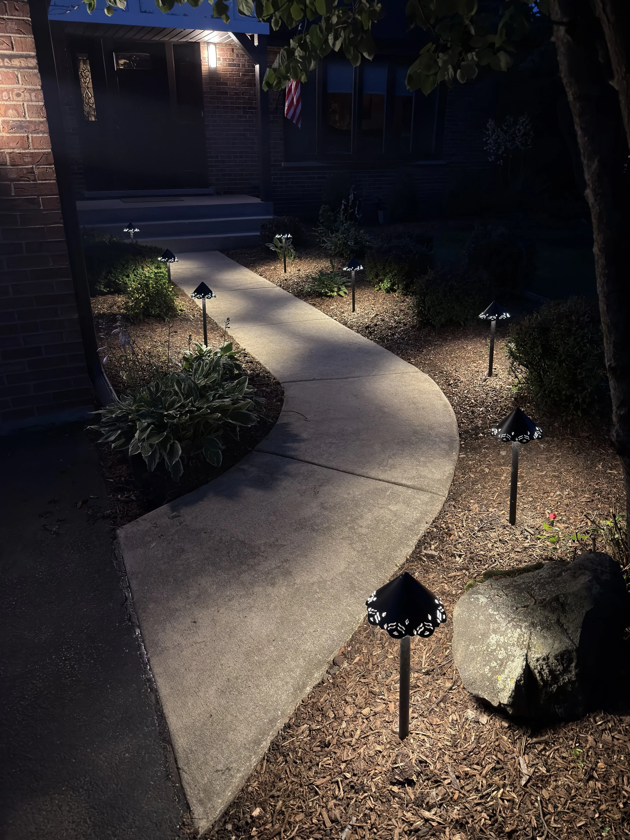 Vertical night view of a curved front walkway highlighted by path lights, decorative rock, and a large boulder.