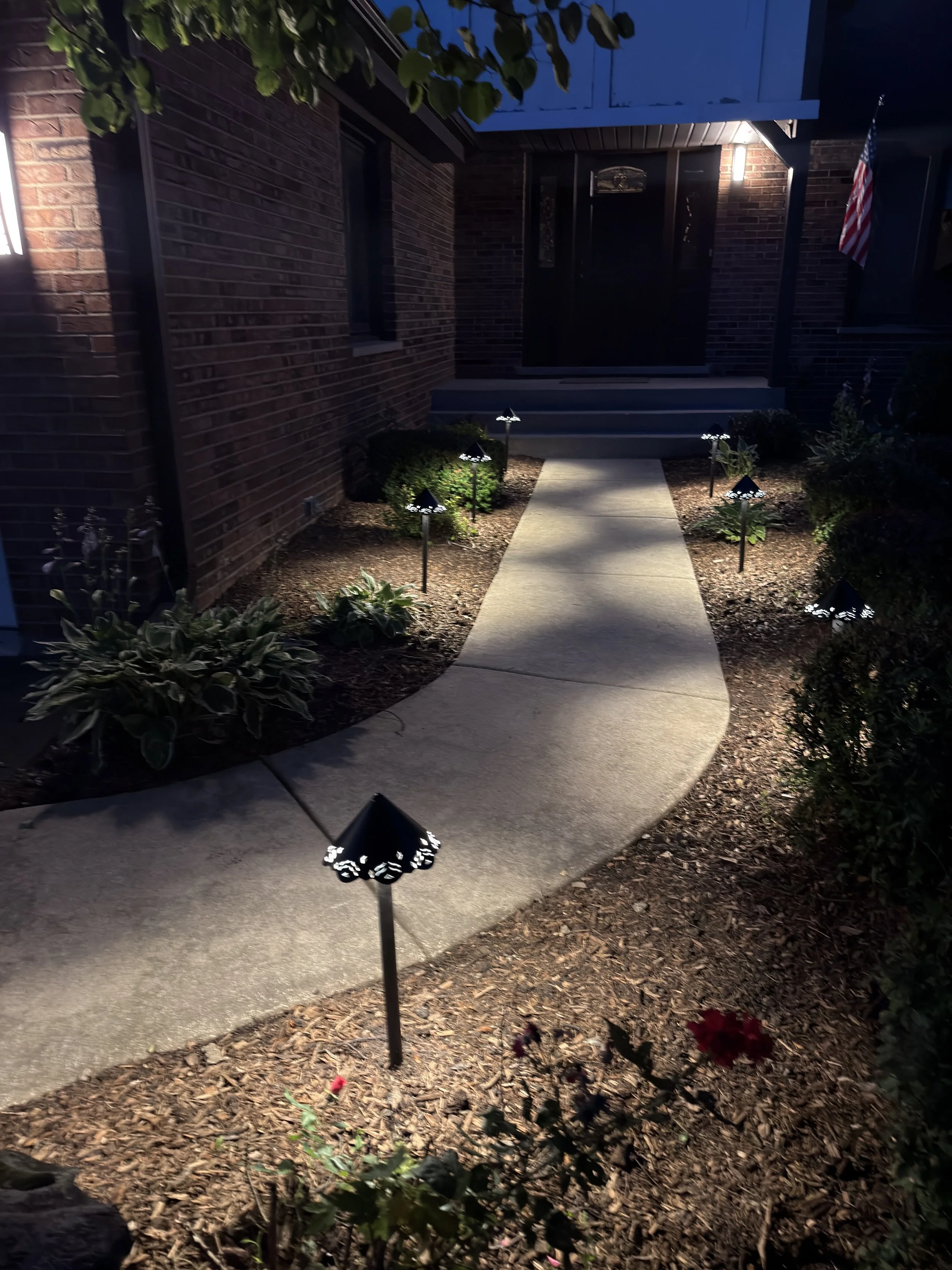 Vertical night view from the opposite side of a curved walkway, showing path lights and the front entry.