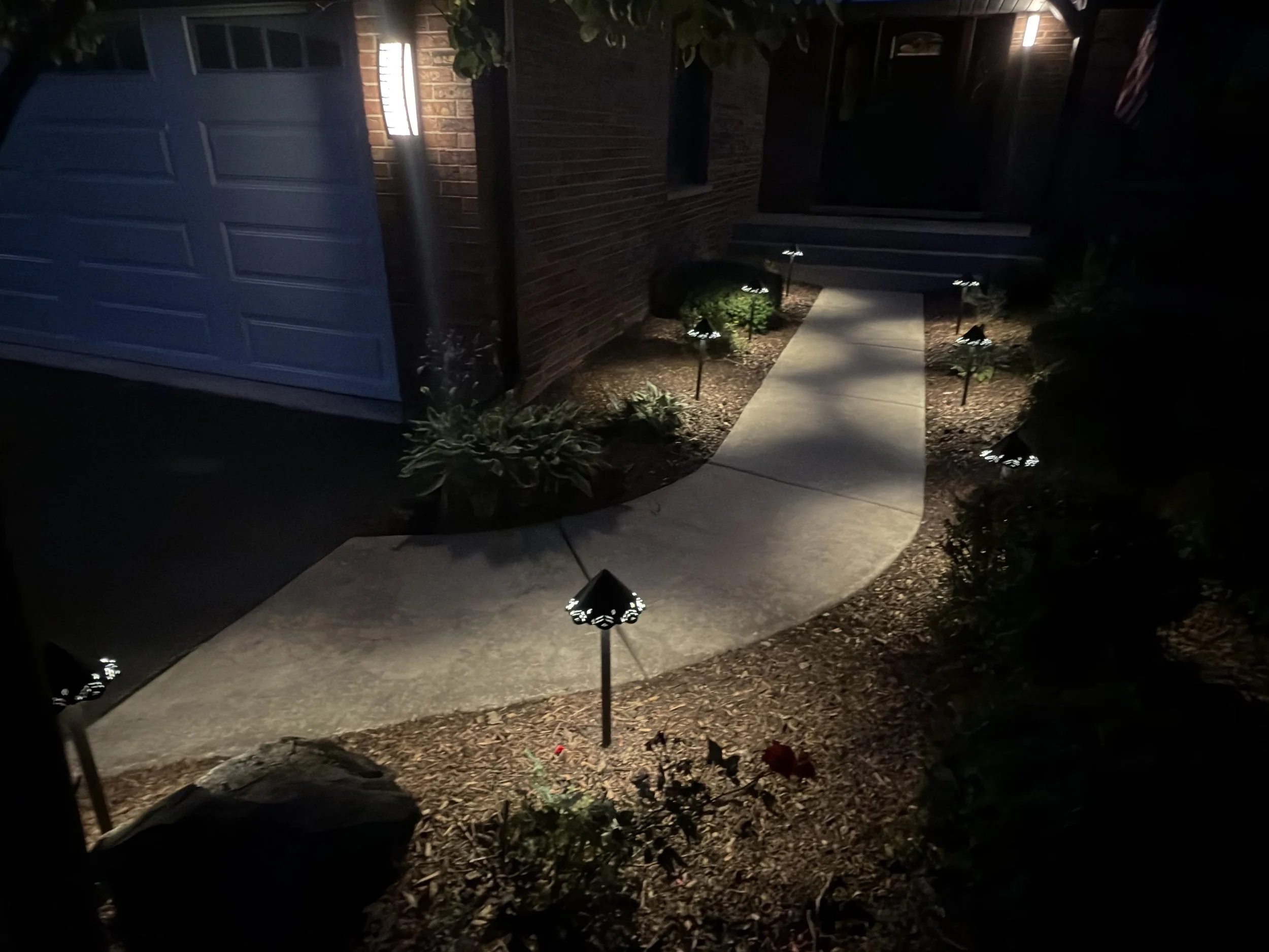 Wide night view of a brick home and landscaped entry illuminated by low-voltage path lights.