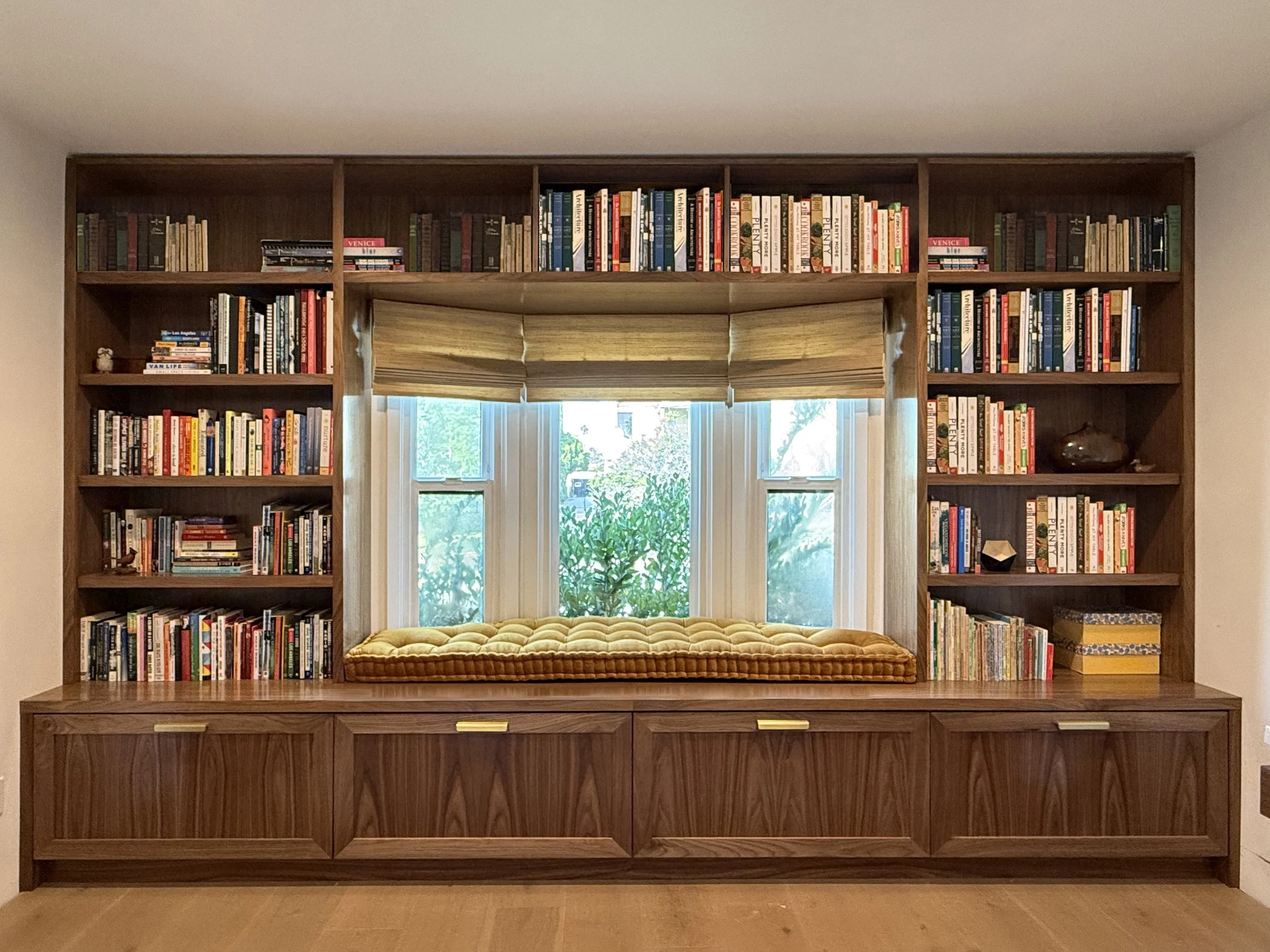 Walnut bookcase with books and a window seat with a cushion, built-in design.