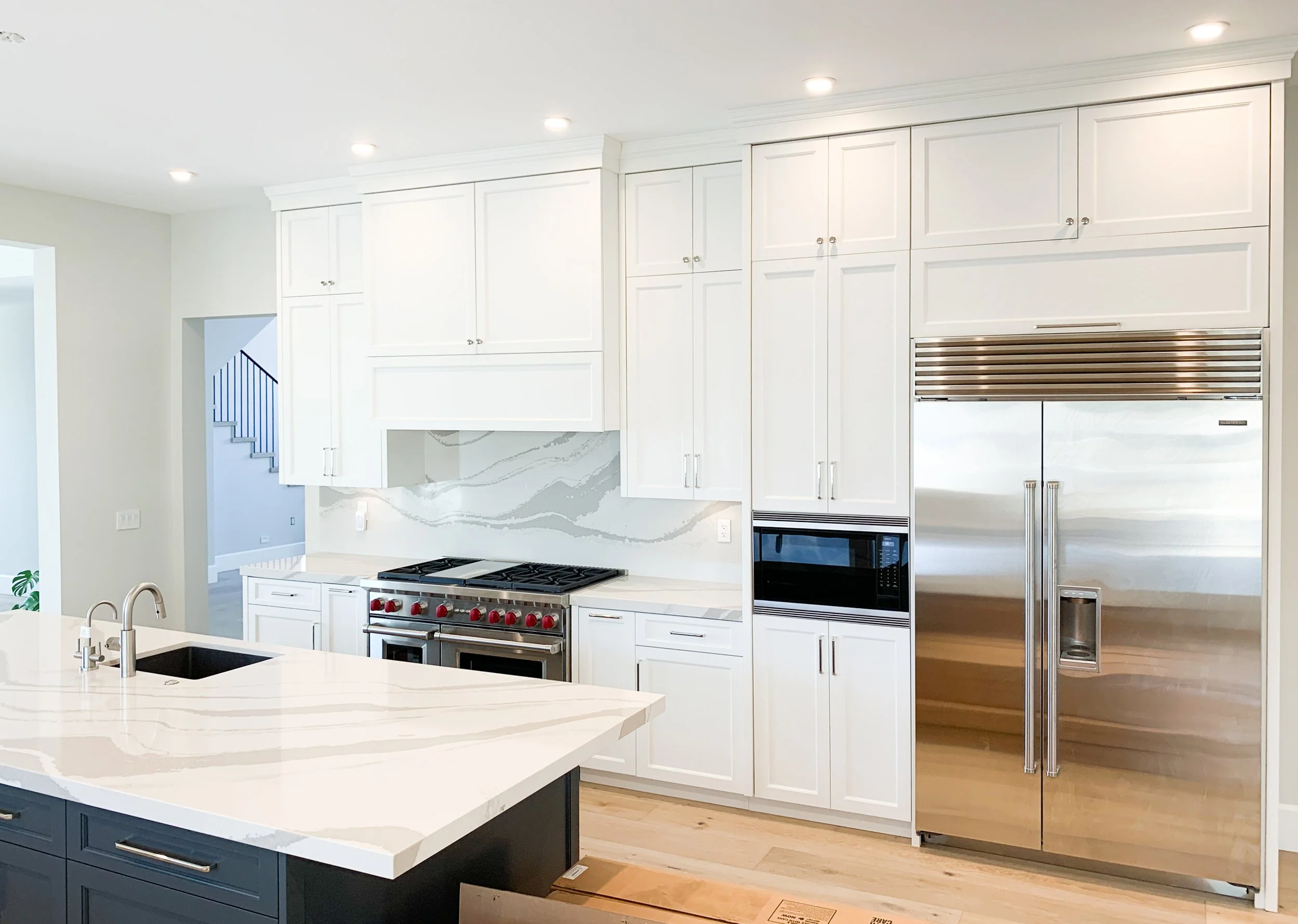 Modern kitchen with white cabinets, stainless steel refrigerator, built-in oven, and an island with a sink and marble countertop.