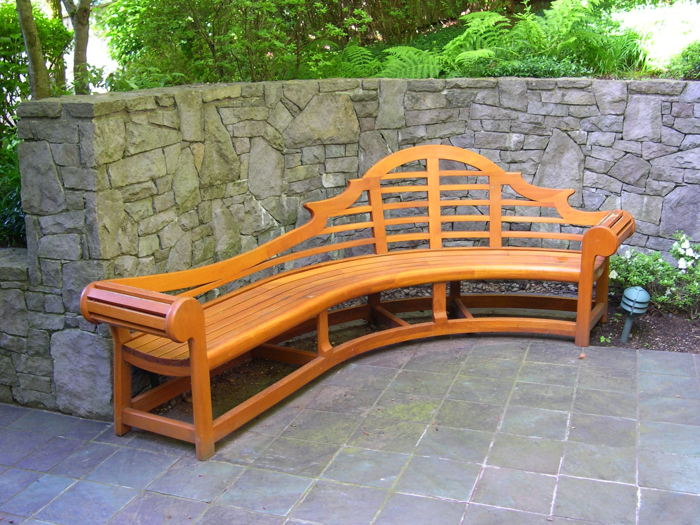 A solid teak garden bench in the style of Edwin Lutyens designed to fit a curved garden wall