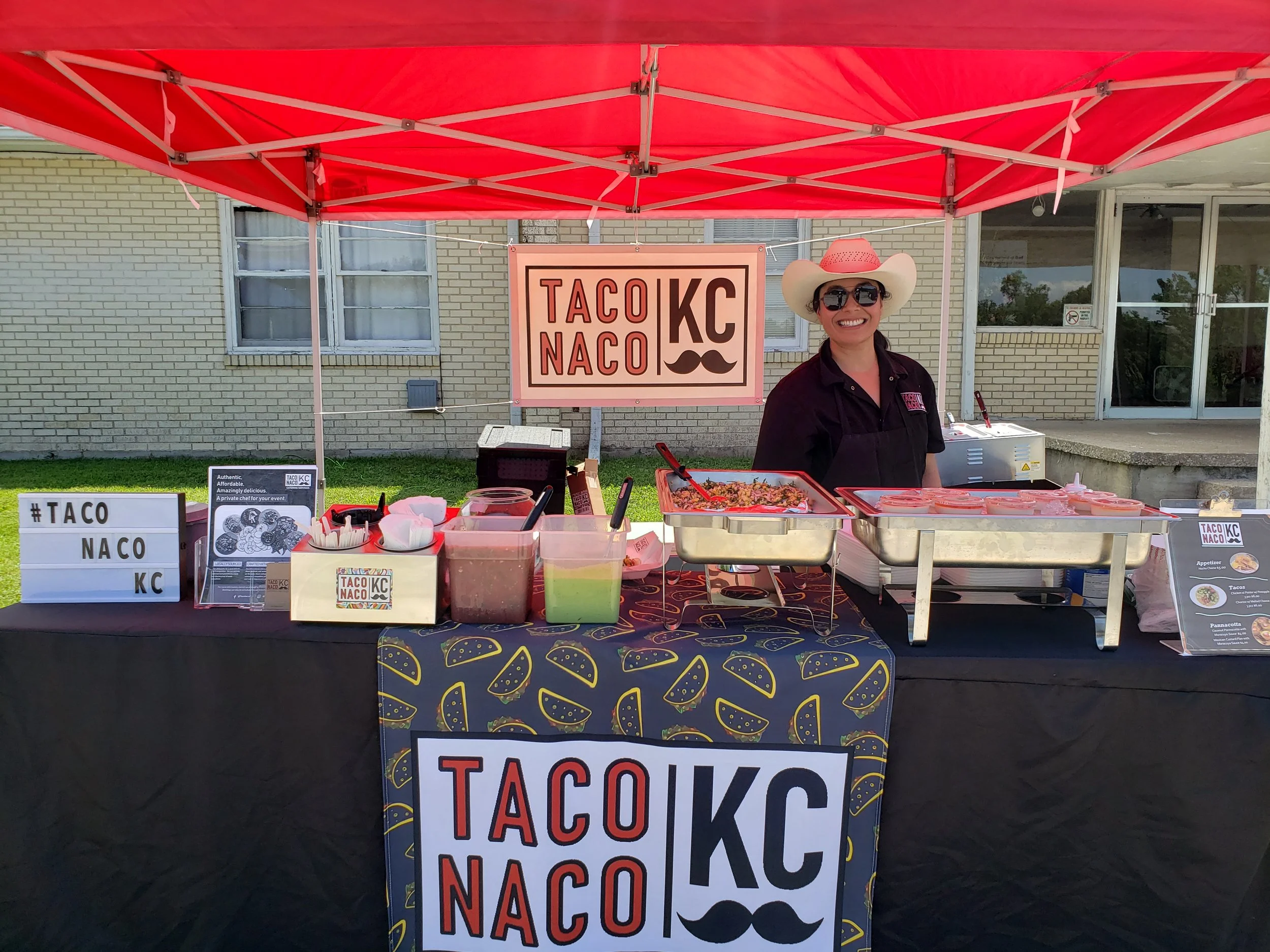 Taco Naco food stand with a smiling vendor in a cowboy hat, taco toppings, and colorful signage under a red canopy.